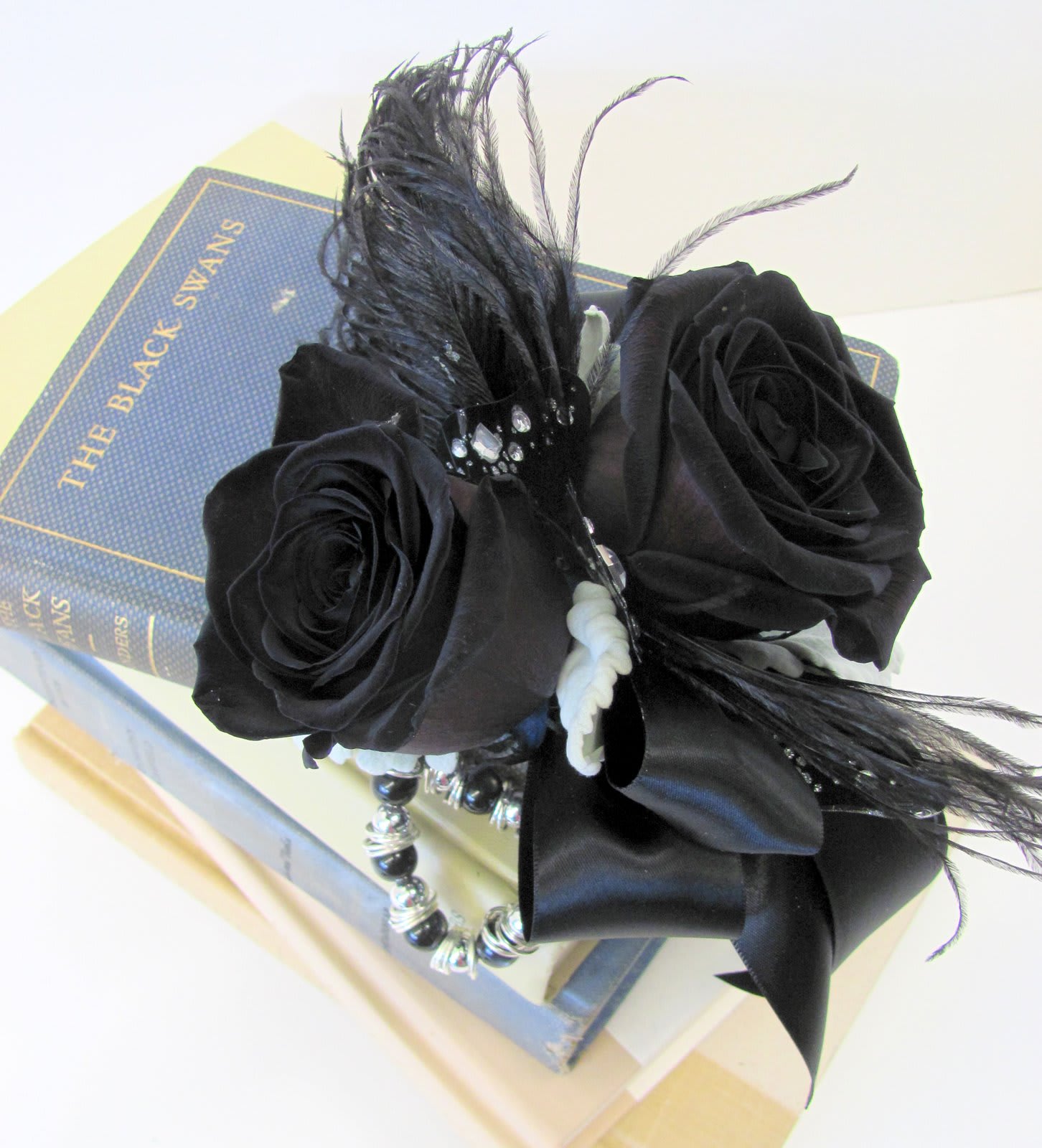Black rose arrangement with feathers and beads on a book box