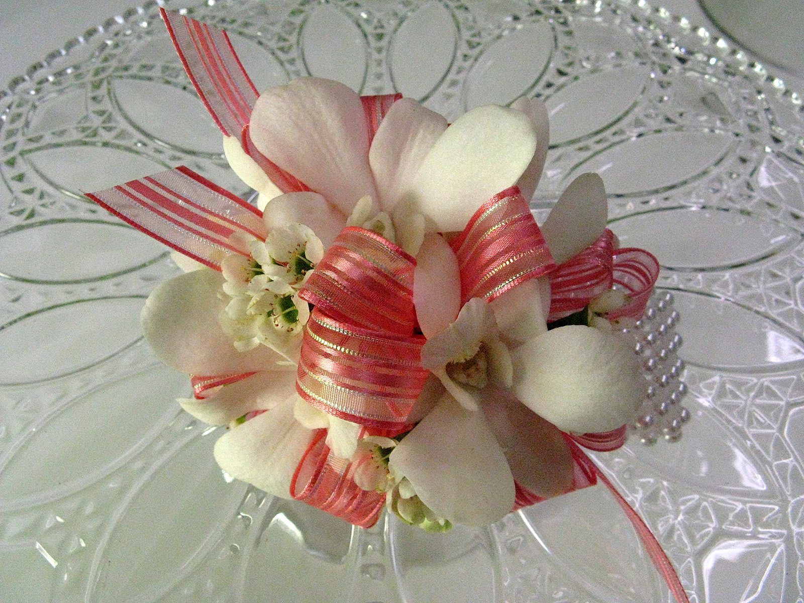 White orchid corsage with pink ribbon on a clear glass plate