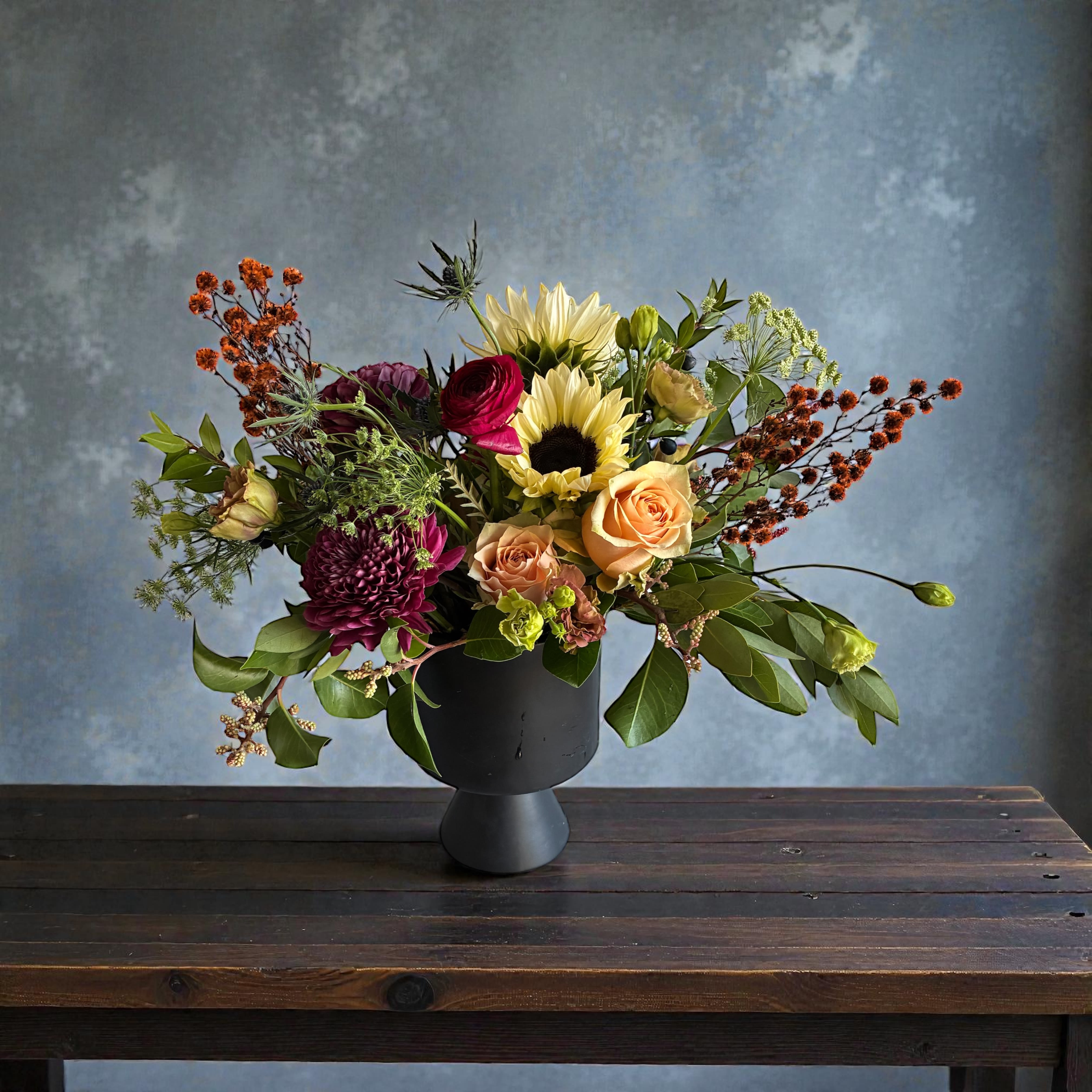 Mixed bouquet in a black vase with sunflowers, roses, and dark blooms