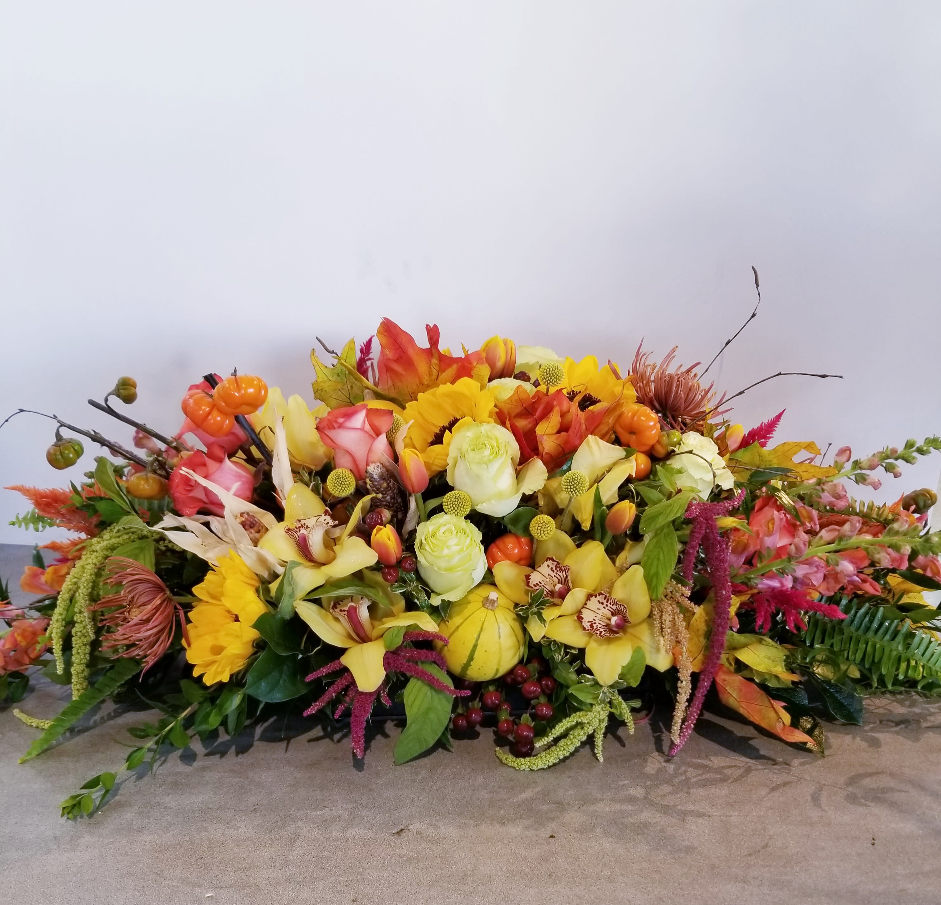 Grand Thanksgiving - This fall favorite is one-of-a-kind, featuring a glorious autumnal roses, orchids, tulips, lilies, gourds, pumpkins and sunflowers beautifully  arranged in a stoneware dish.  This grand arrangement is approximately: 30" long x 8" tall x 8" wide. 