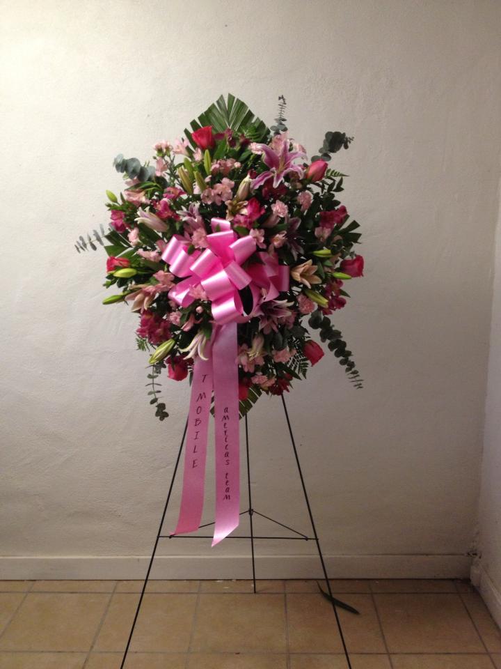 Pink and white funeral spray on a stand with a large pink ribbon