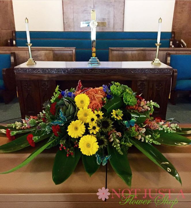 Large floral arrangement with yellow daisies and orange roses in front of a church altar