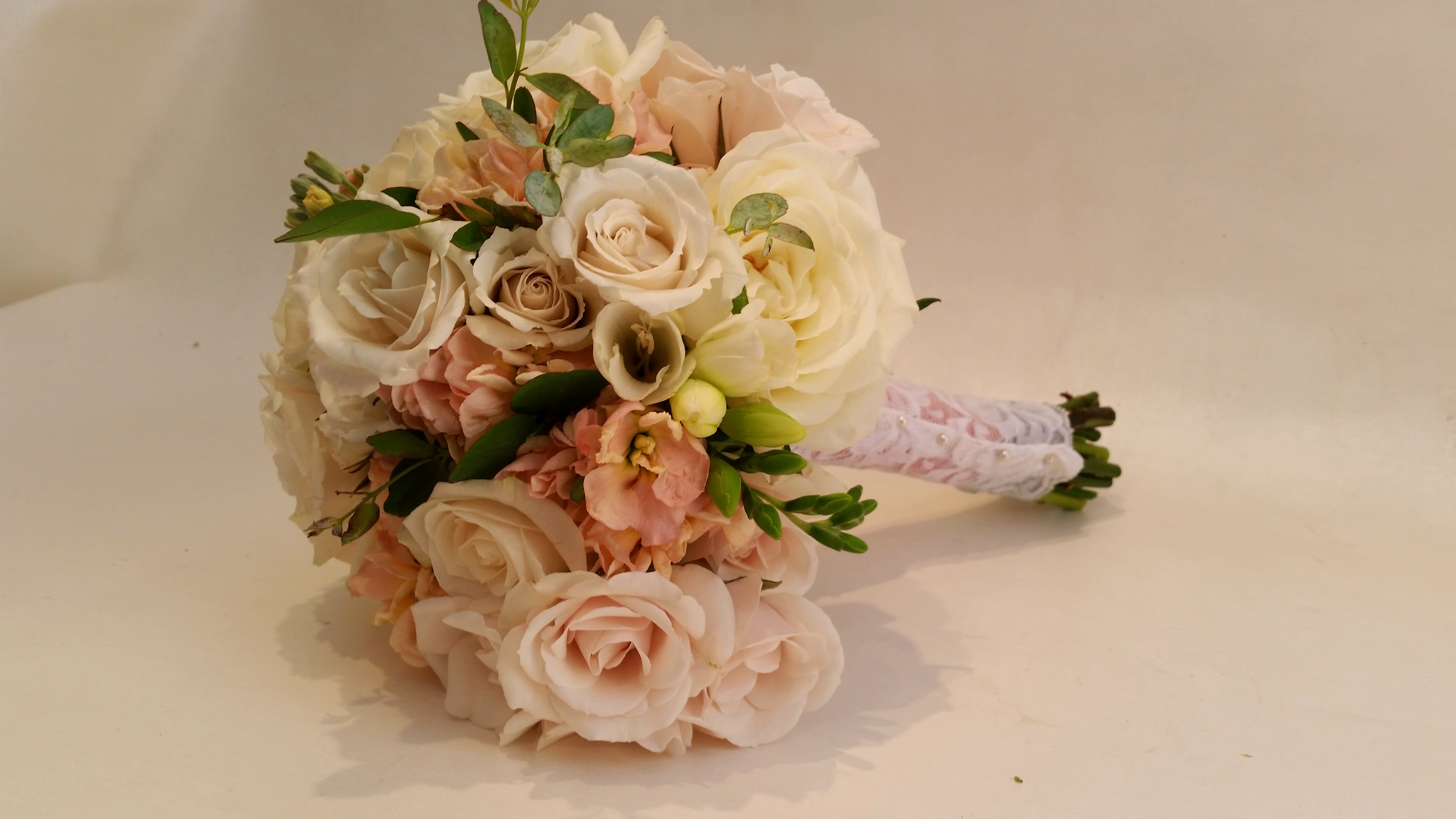 Bouquet of pale roses and peach flowers with greenery, wrapped in lace