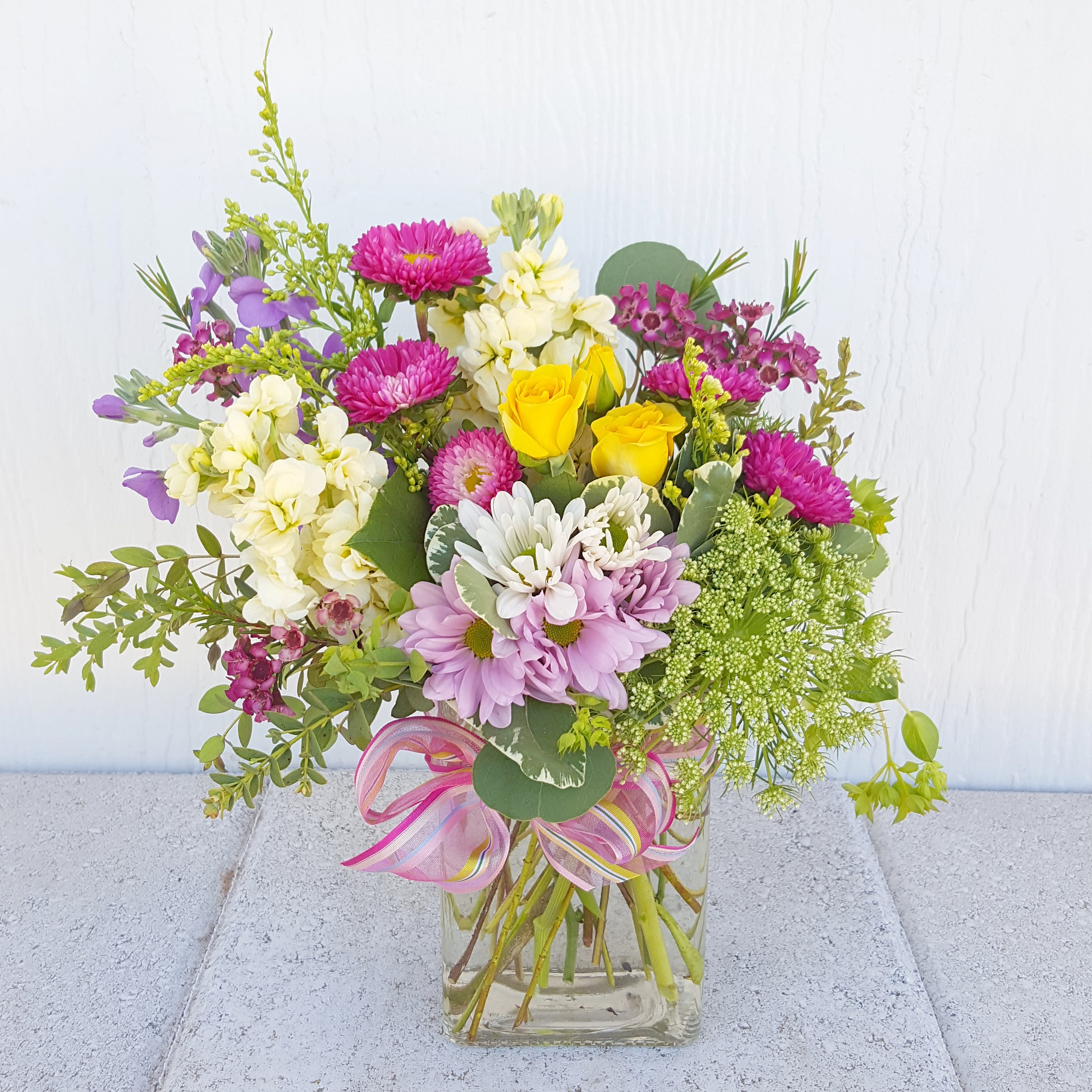 Mixed bouquet of pink, yellow, white, and purple flowers in a glass vase