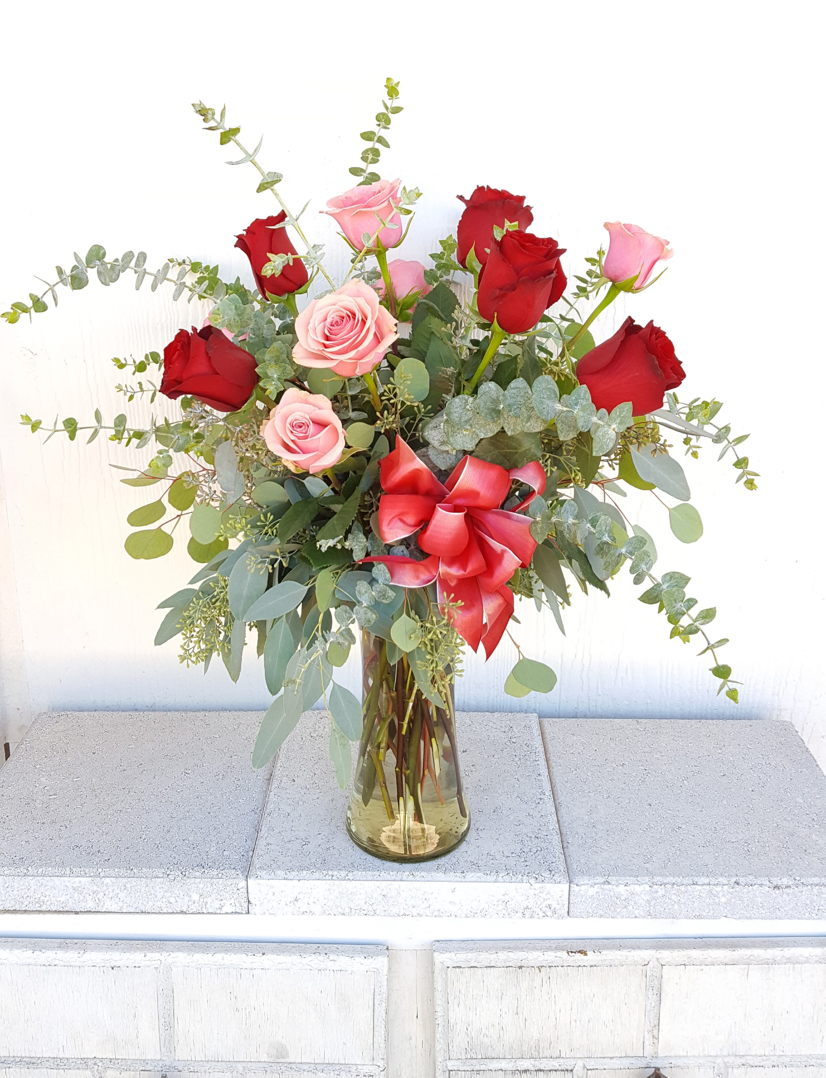 Red and pink roses in a glass vase with a red ribbon