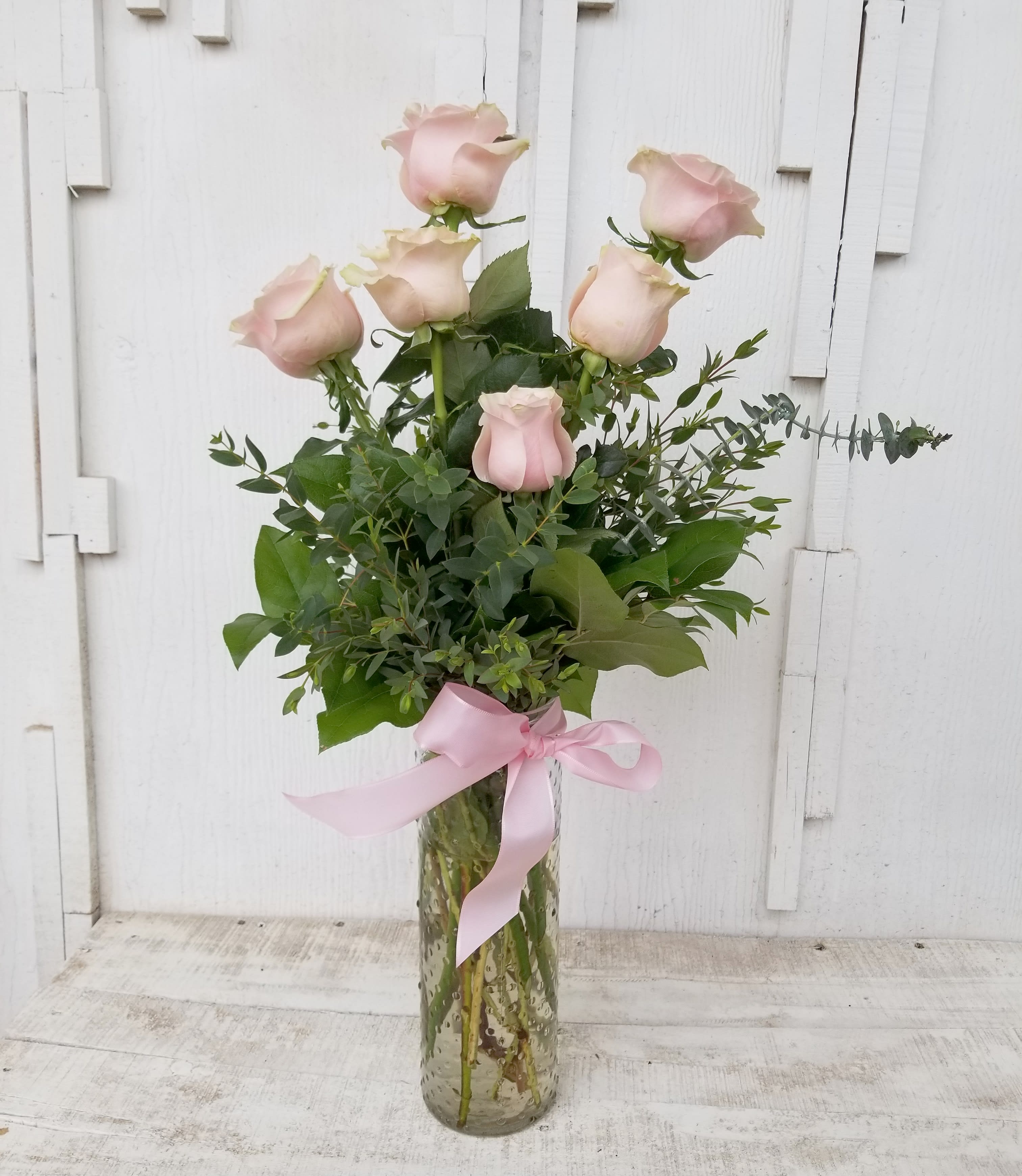 Tall bouquet of pale pink roses in a glass vase with a pink ribbon