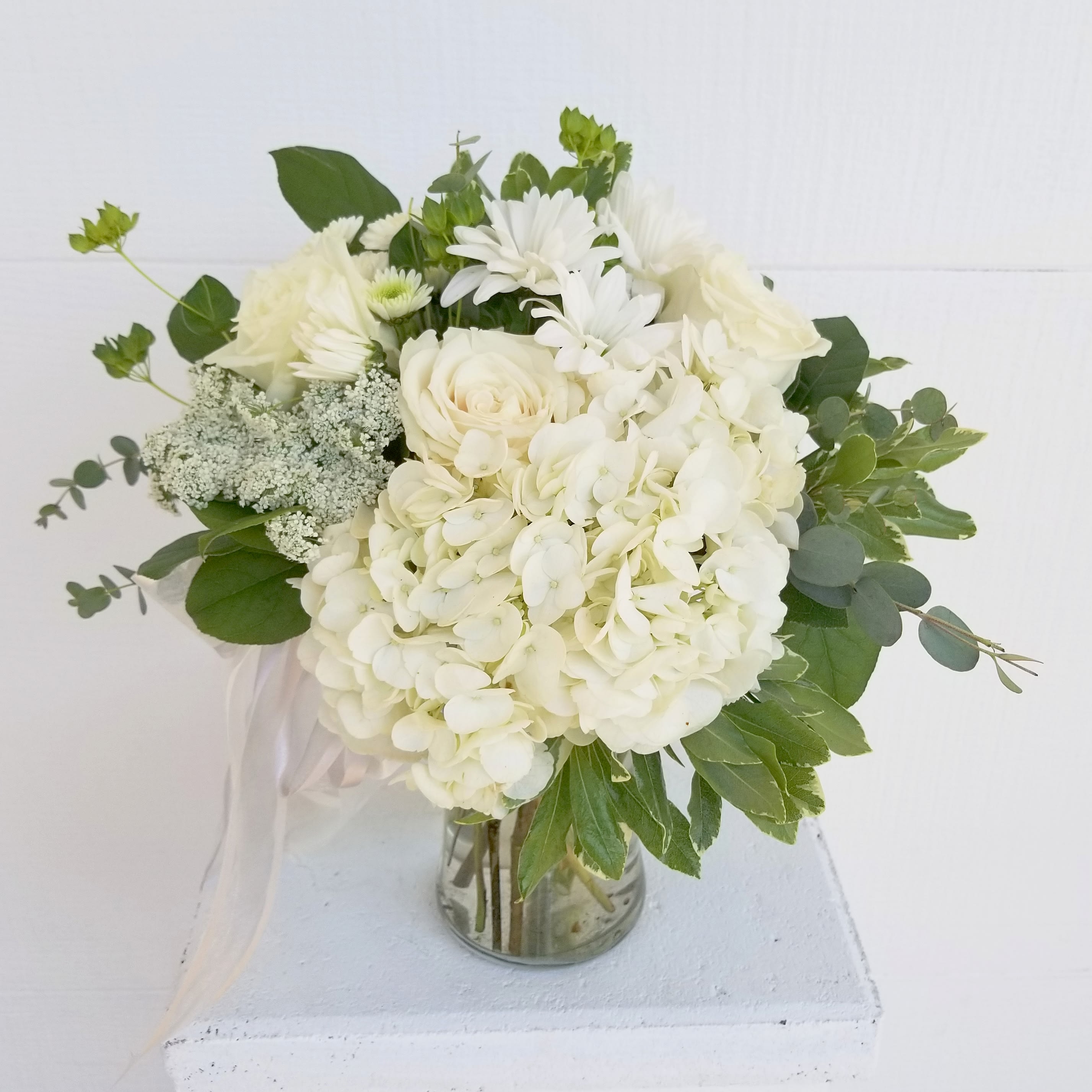 White floral bouquet in a glass vase with green foliage