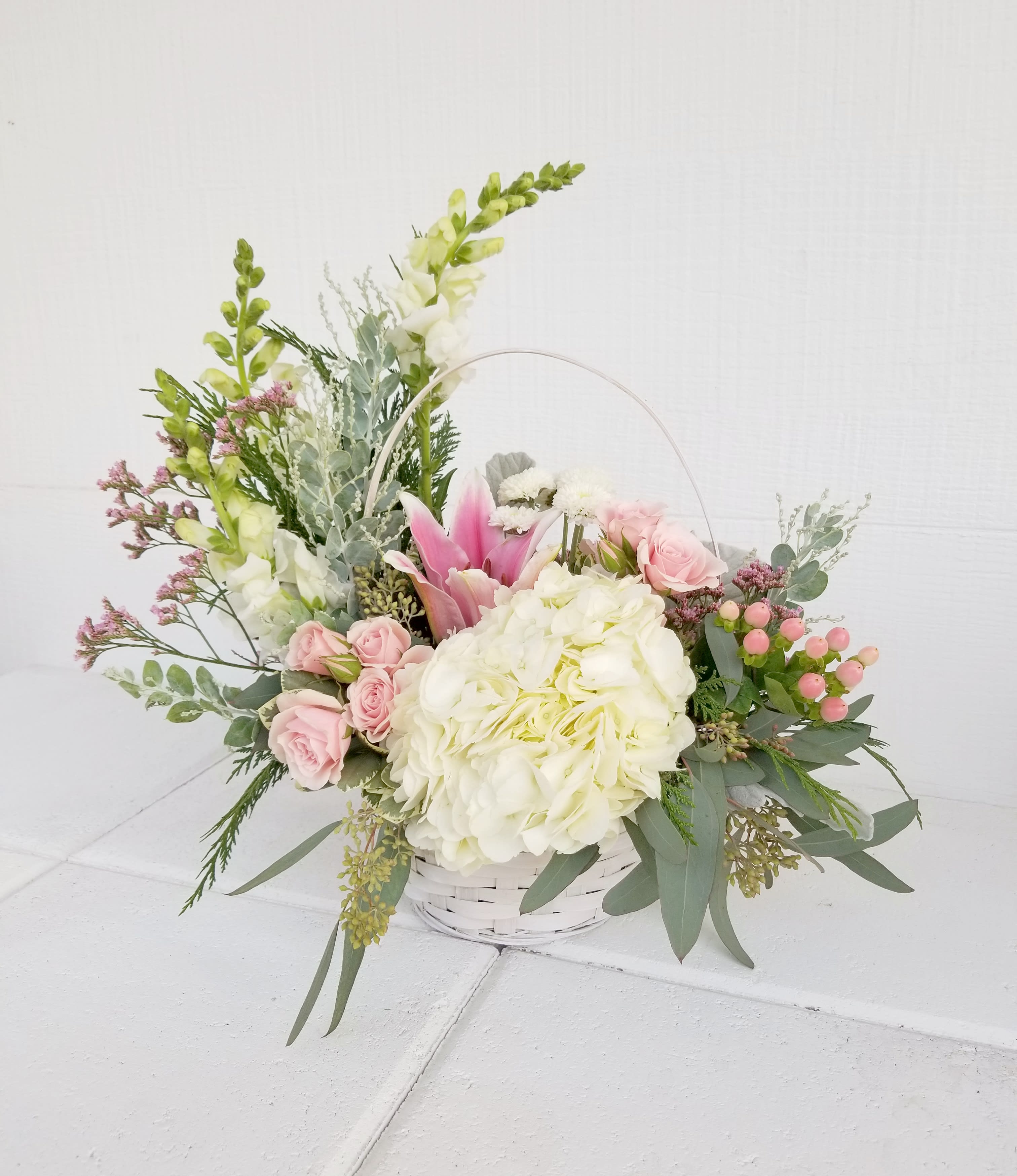 Basket arrangement with pink roses, white hydrangea, and tall white blooms
