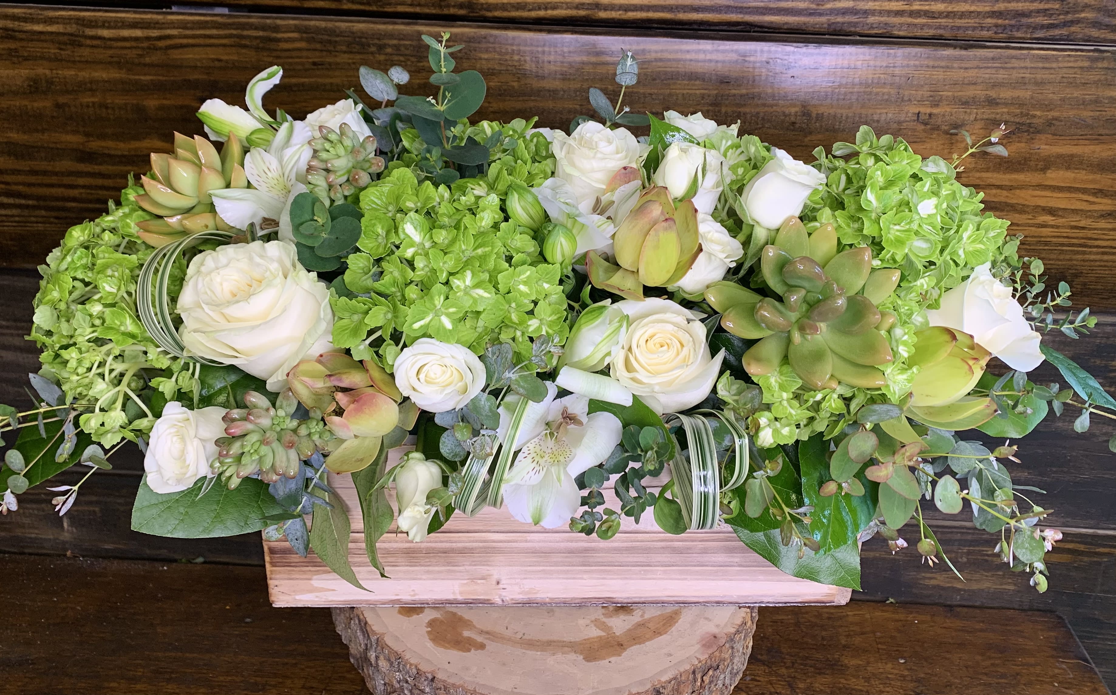 Low floral centerpiece with white roses, green hydrangeas, and succulents in a wooden box