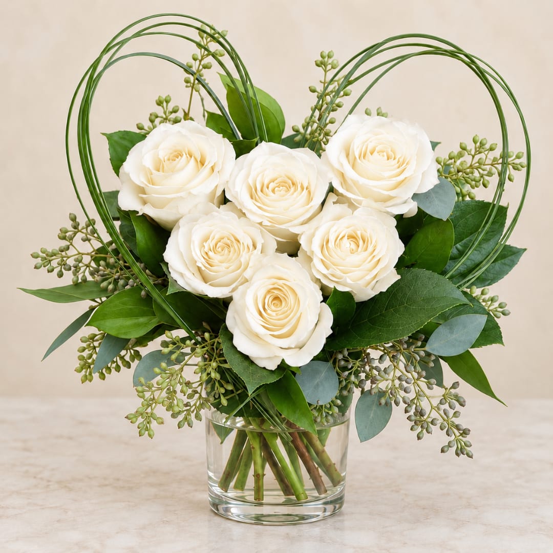White roses arranged in a glass vase with looping green wire accents
