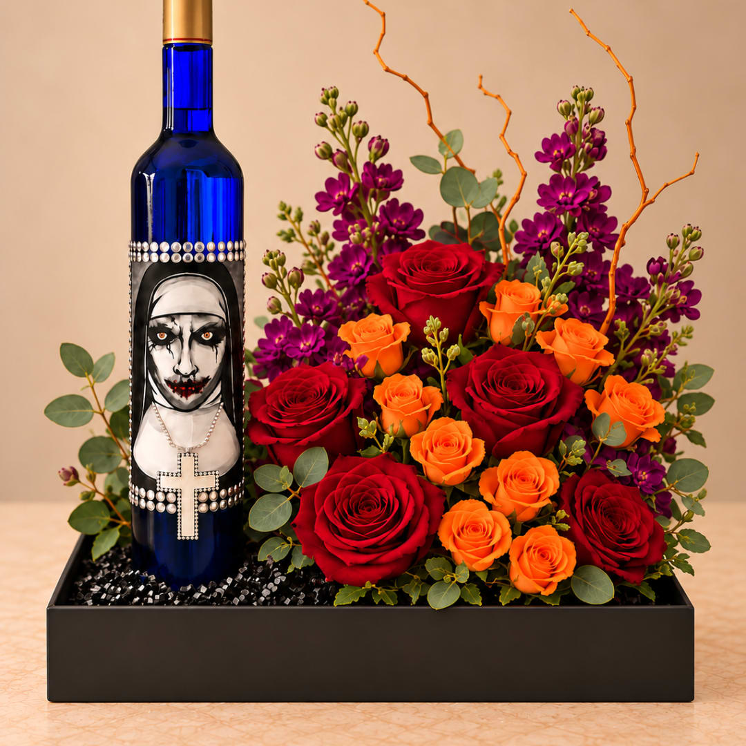 Red and orange roses with purple flowers arranged beside a decorated blue bottle