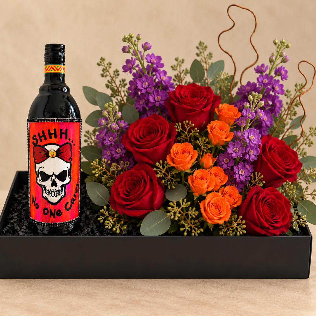 Red and orange roses with purple flowers in a black gift box beside a decorated bottle