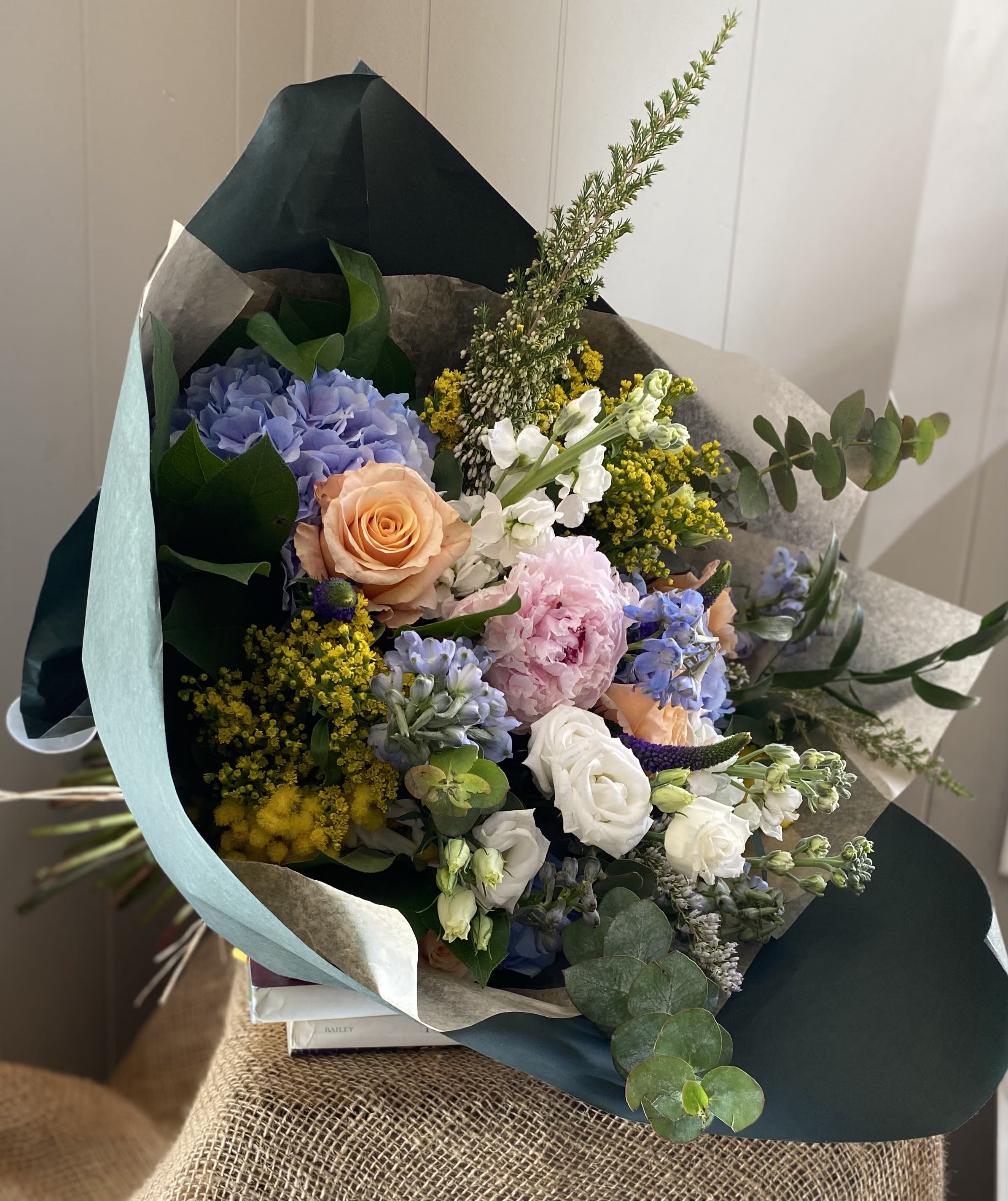 Mixed bouquet with hydrangea, roses, and pastel blooms wrapped in dark paper