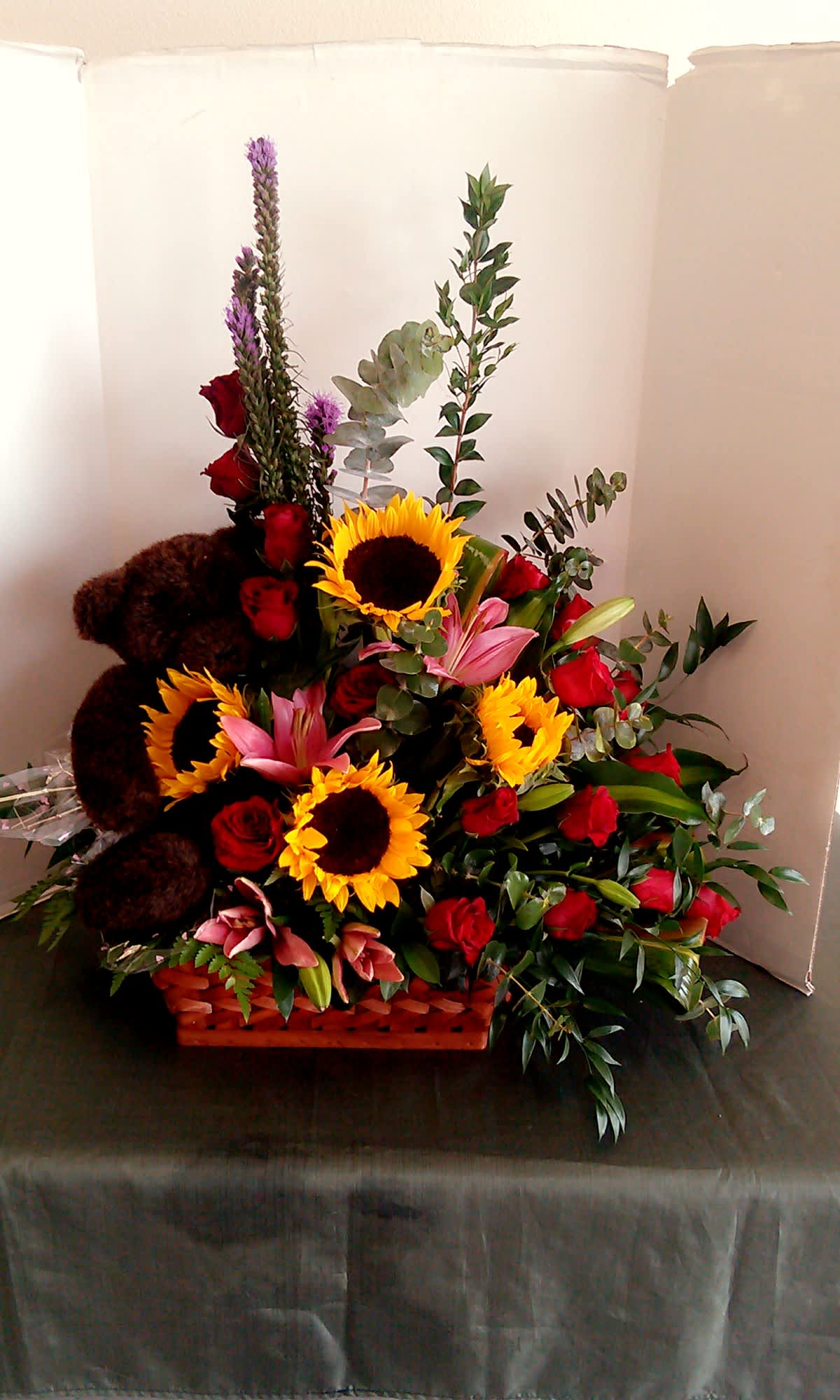 Basket arrangement with sunflowers, red roses, pink lilies, and a teddy bear
