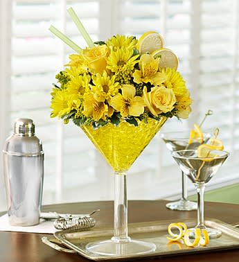 Lemon Martini Bouquet - Product ID: 91078  EXCLUSIVE Send sunny sophistication with our truly original Happy Hour bouquet, inspired by the famous Lemon Drop Martini. Our floral version of the cosmopolitan cocktail is hand-crafted inside an oversized acrylic martini glass from cheerful yellow roses, daisies, alstroemeria and solidago. Topped with a faux lemon slice garnish, it's enough to fill anyone with sunshine and smiles. Hand-designed, bright arrangement of roses, daisy poms, alstroemeria, solidago and variegated pittosporum Arrives in a reusable, oversized acrylic martini glass; measures 10.5"H Accented with a realistic lemon slice garnish Extra Large arrangement measures approximately 14"H x 9"L Large arrangement measures approximately 13"H x 8.5"L Medium arrangement measures approximately 12"H x 8"L Small arrangement measures approximately 12"H x 7"L Our florists select the freshest flowers available so colors and varieties may vary