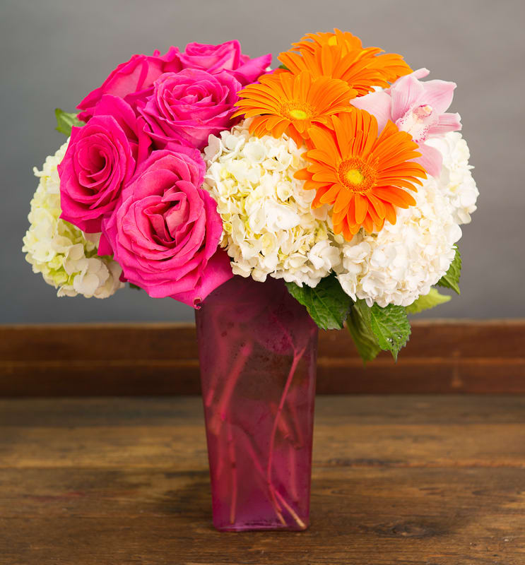 Pink roses and orange gerbera daisies in a tall magenta vase
