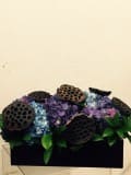 Dark floral arrangement with purple and blue blooms in a black container