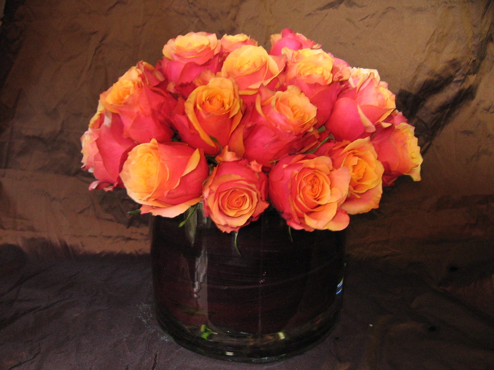 Pink and orange roses arranged in a dark glass vase