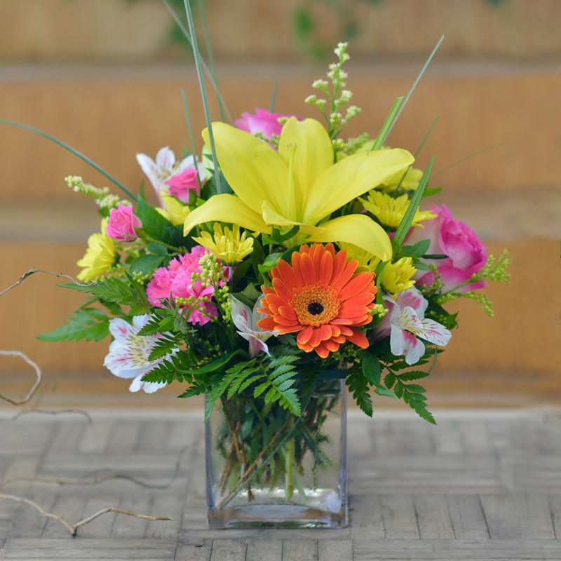 Mixed bouquet with yellow lilies, orange gerbera daisy, and pink flowers in a glass vase