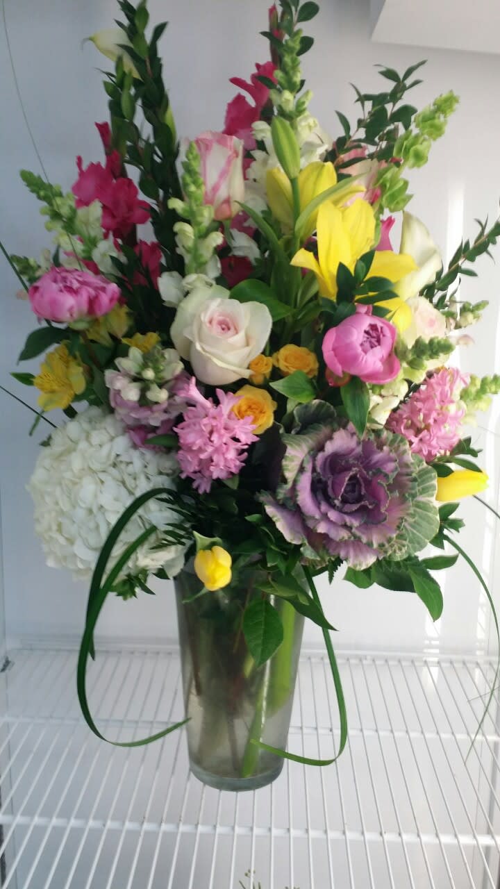 Tall mixed bouquet in a clear glass vase with pink, yellow, white, and purple flowers