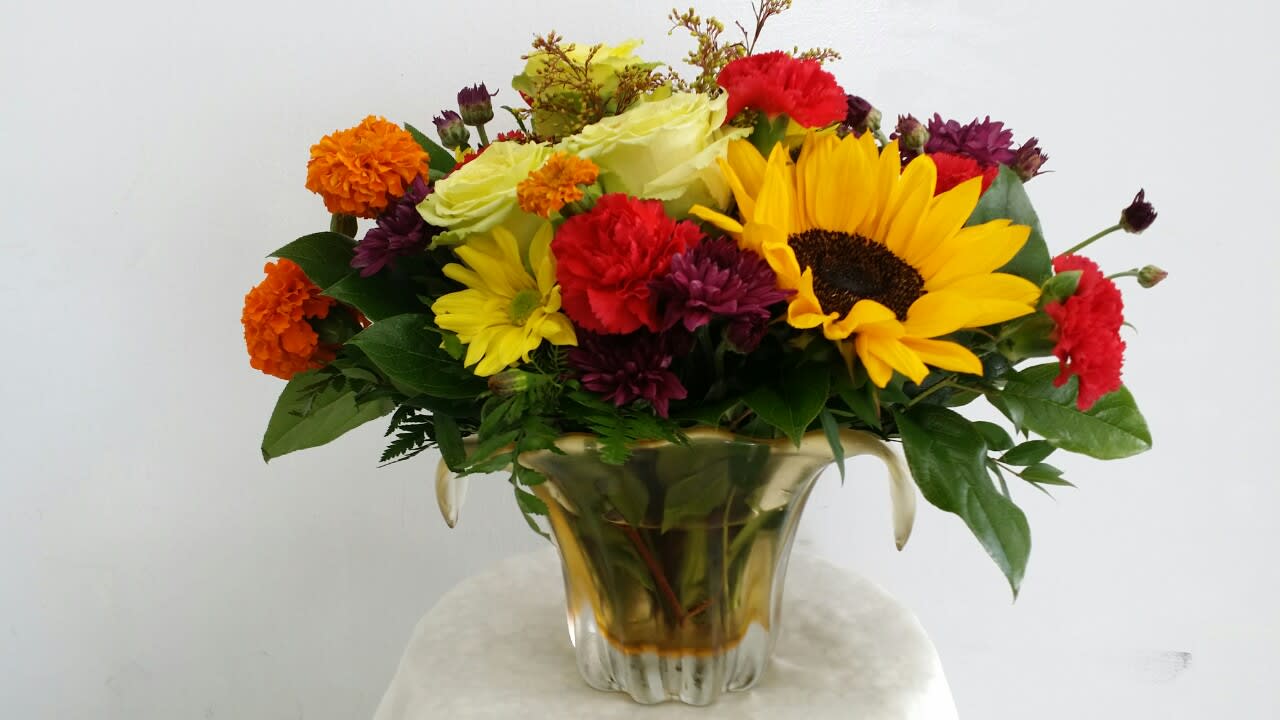 Mixed bouquet with sunflowers, roses, and carnations in a gold vase