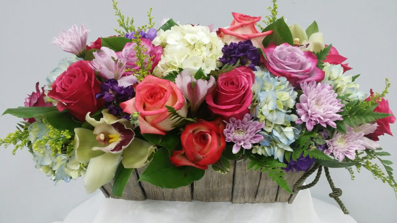 Mixed bouquet of roses, hydrangeas, and orchids in a rustic wooden basket