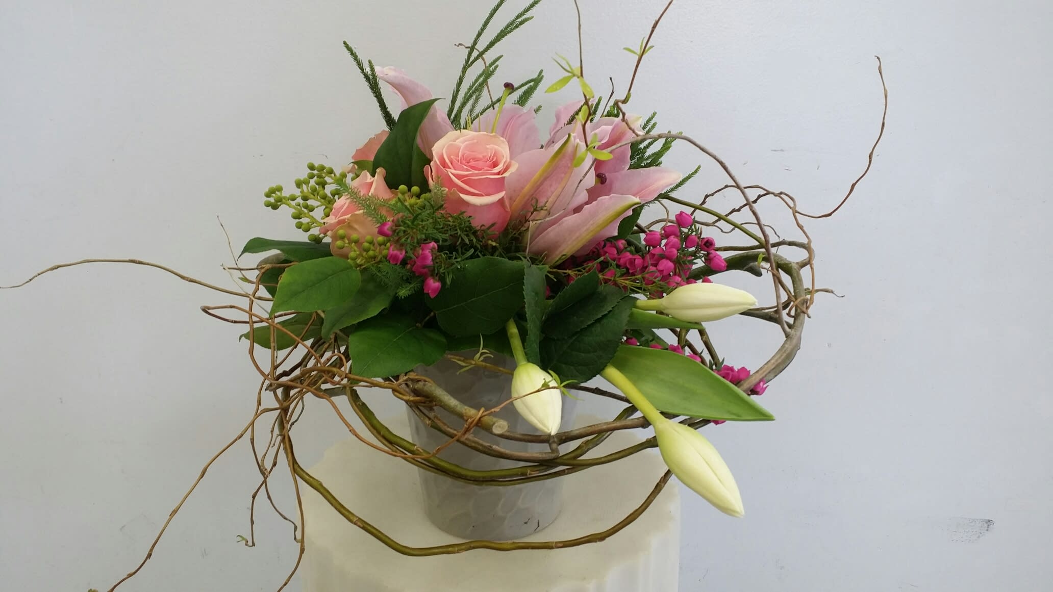 Pink roses and lilies in a glass vase with curly branches