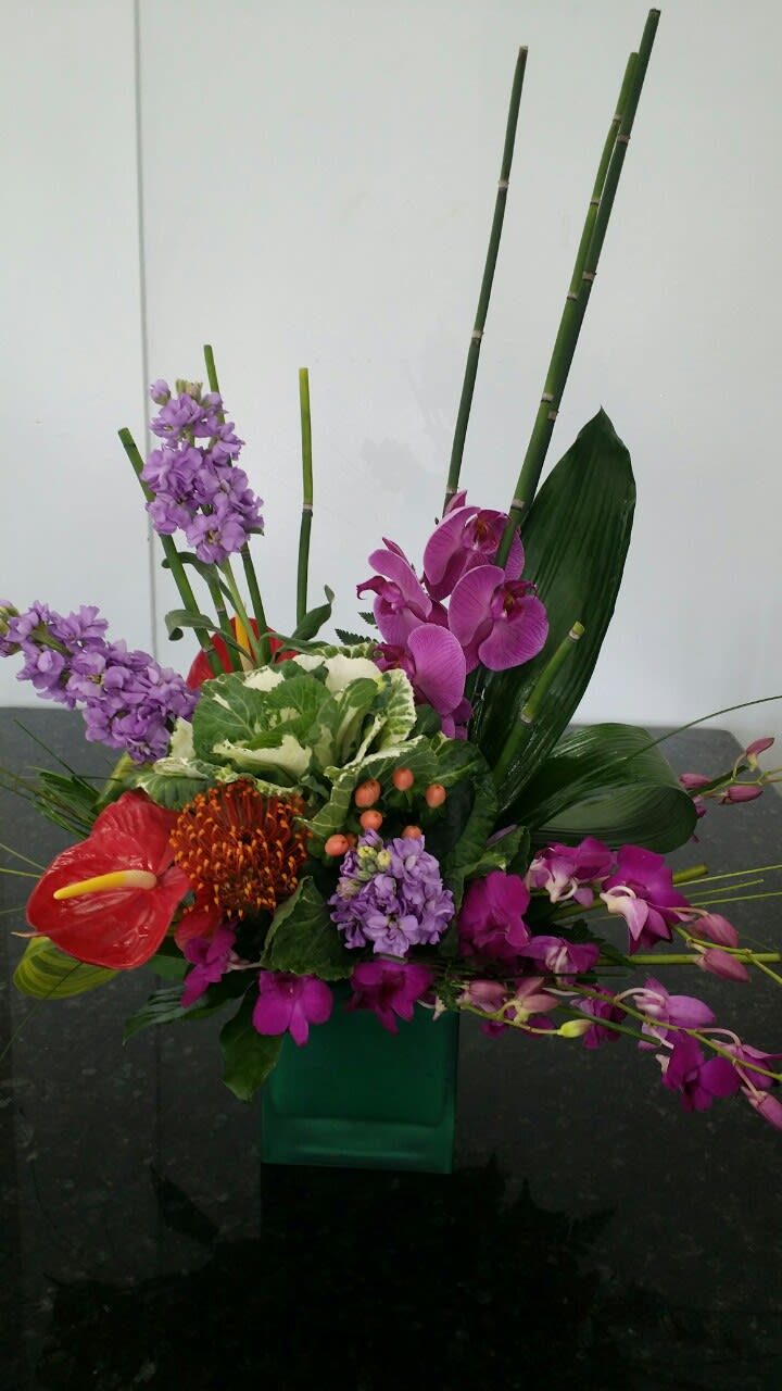 Tropical floral arrangement with orchids and anthurium in a green vase