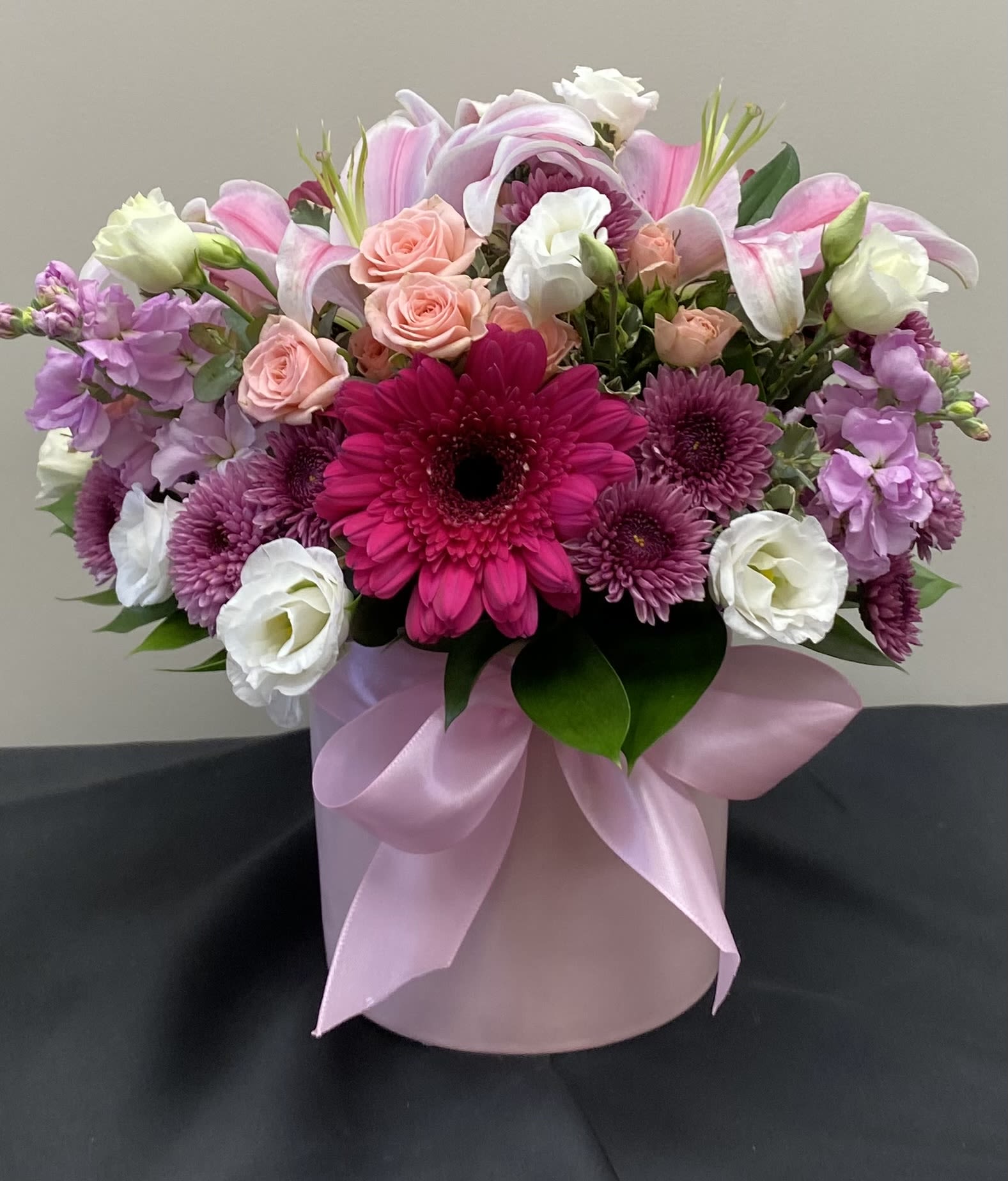 Pink and white mixed flower arrangement in a round pink box with ribbon