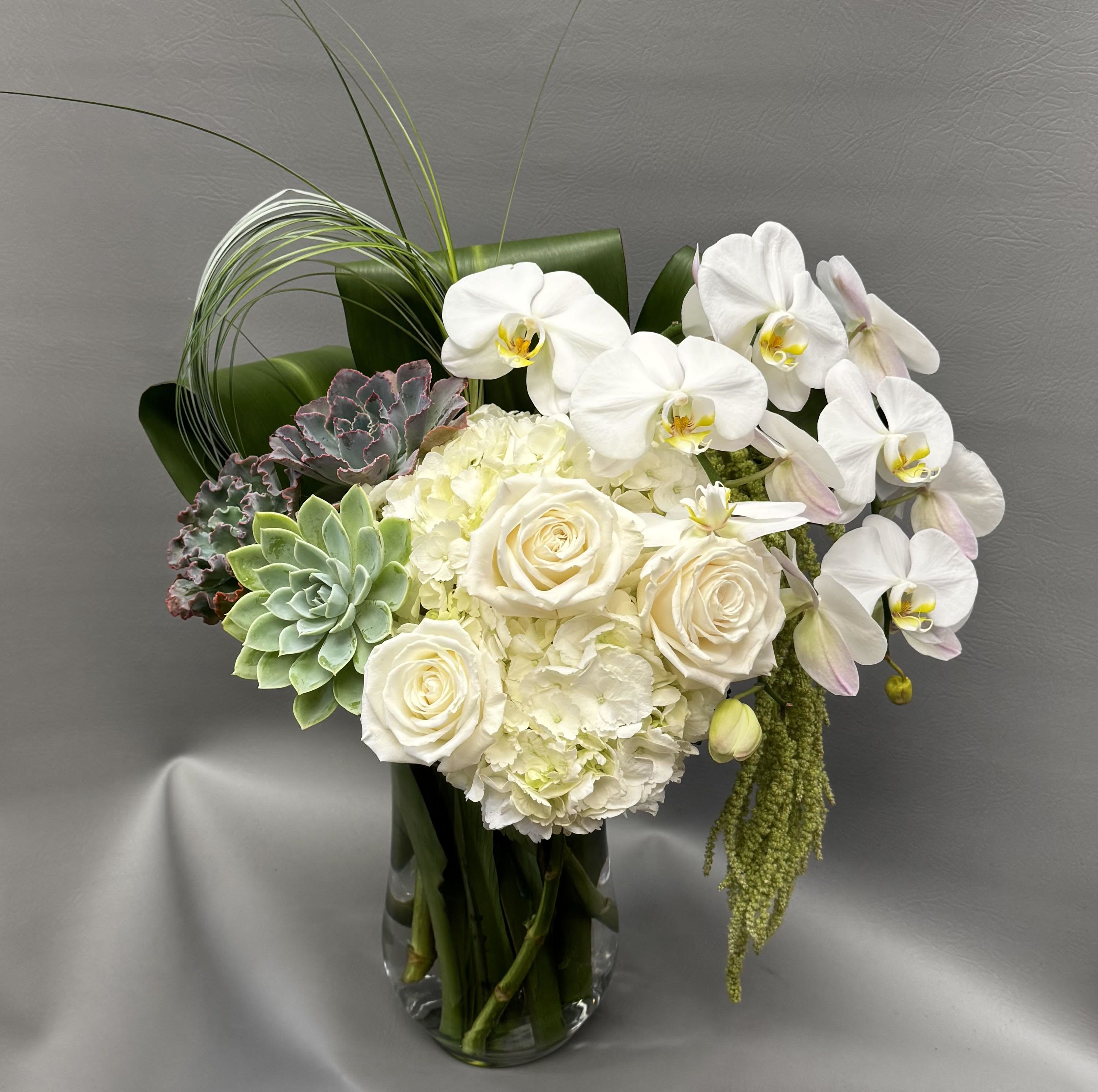 White orchids, roses, hydrangea, and succulents in a clear glass vase