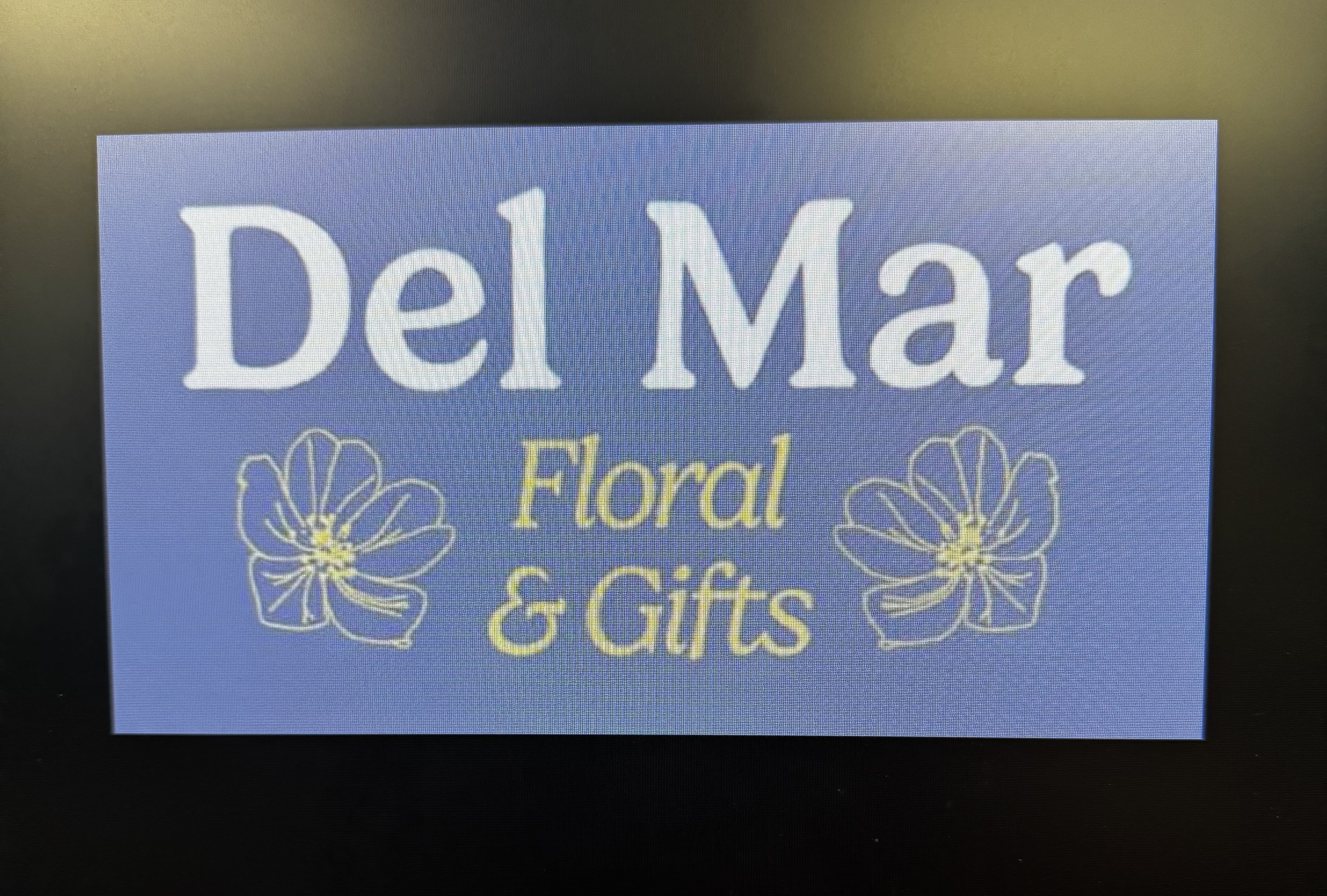 Blue sign reading Del Mar Floral &amp; Gifts with flower outlines
