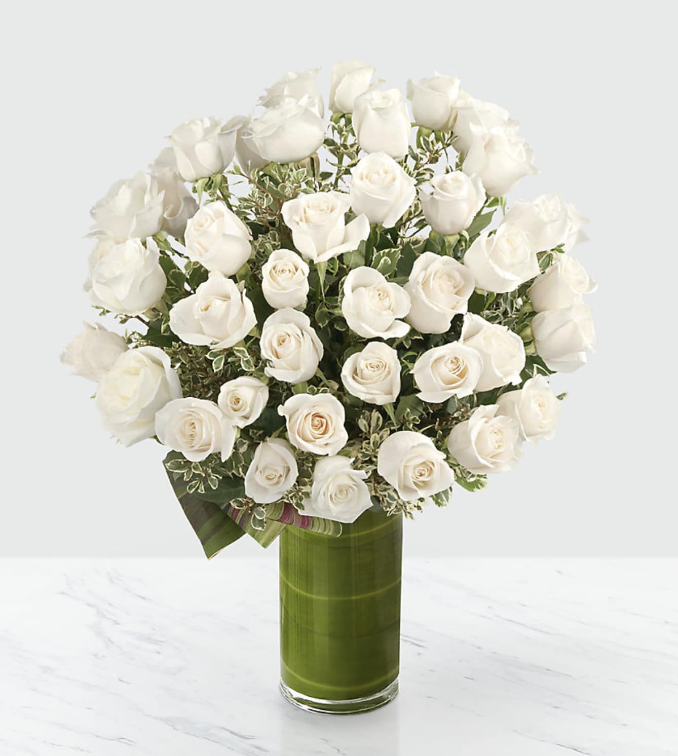 White roses arranged in a tall green glass vase