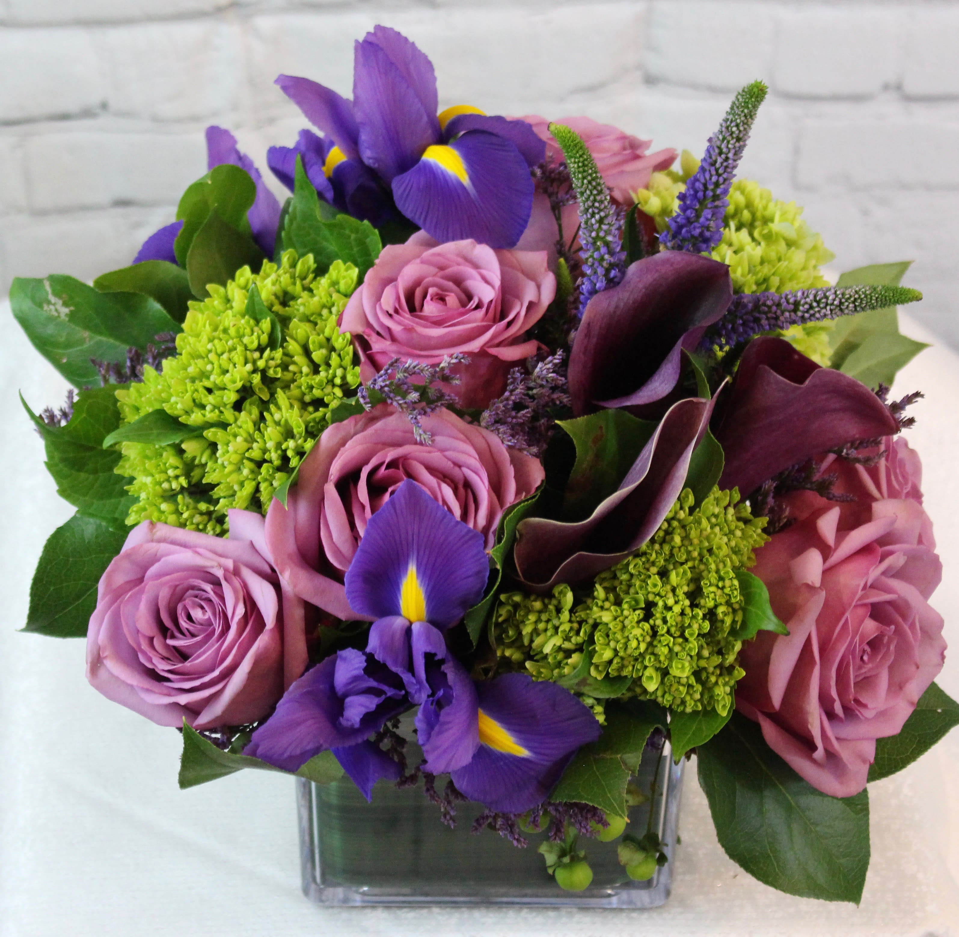 Bouquet of pink roses, purple irises, and green blooms in a glass vase