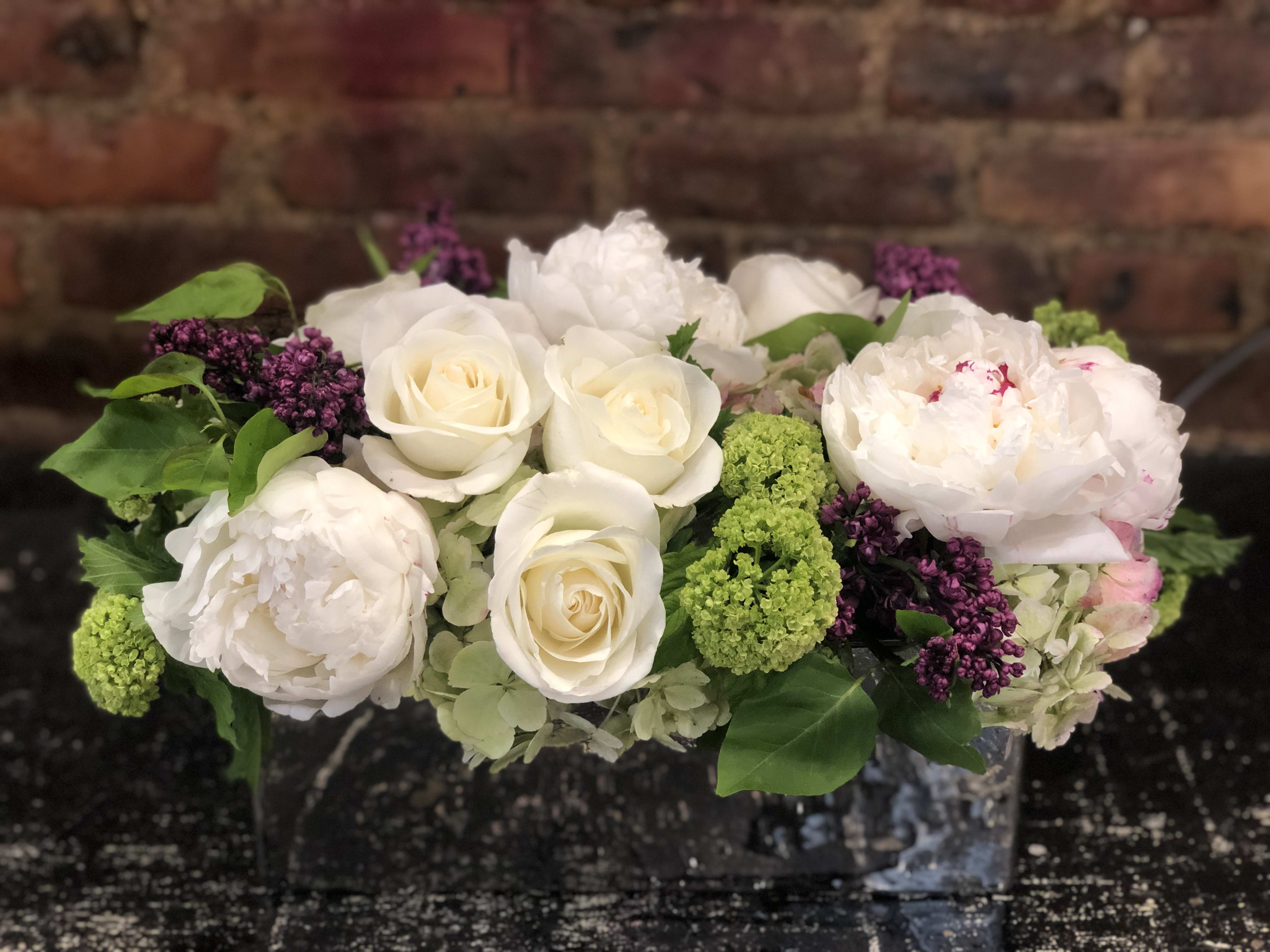White roses and peonies with green and purple accents in a low arrangement