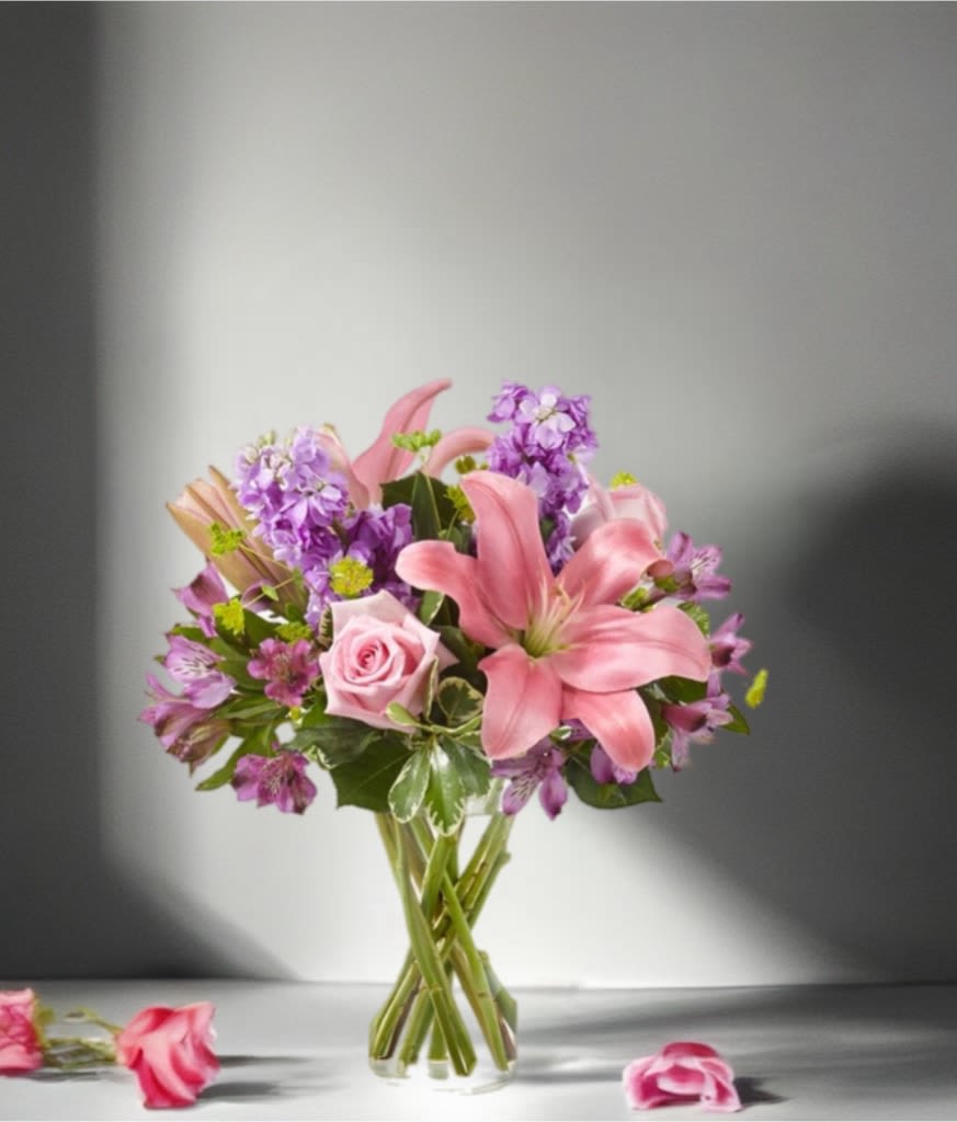 Pink lilies and roses with purple flowers in a clear glass vase