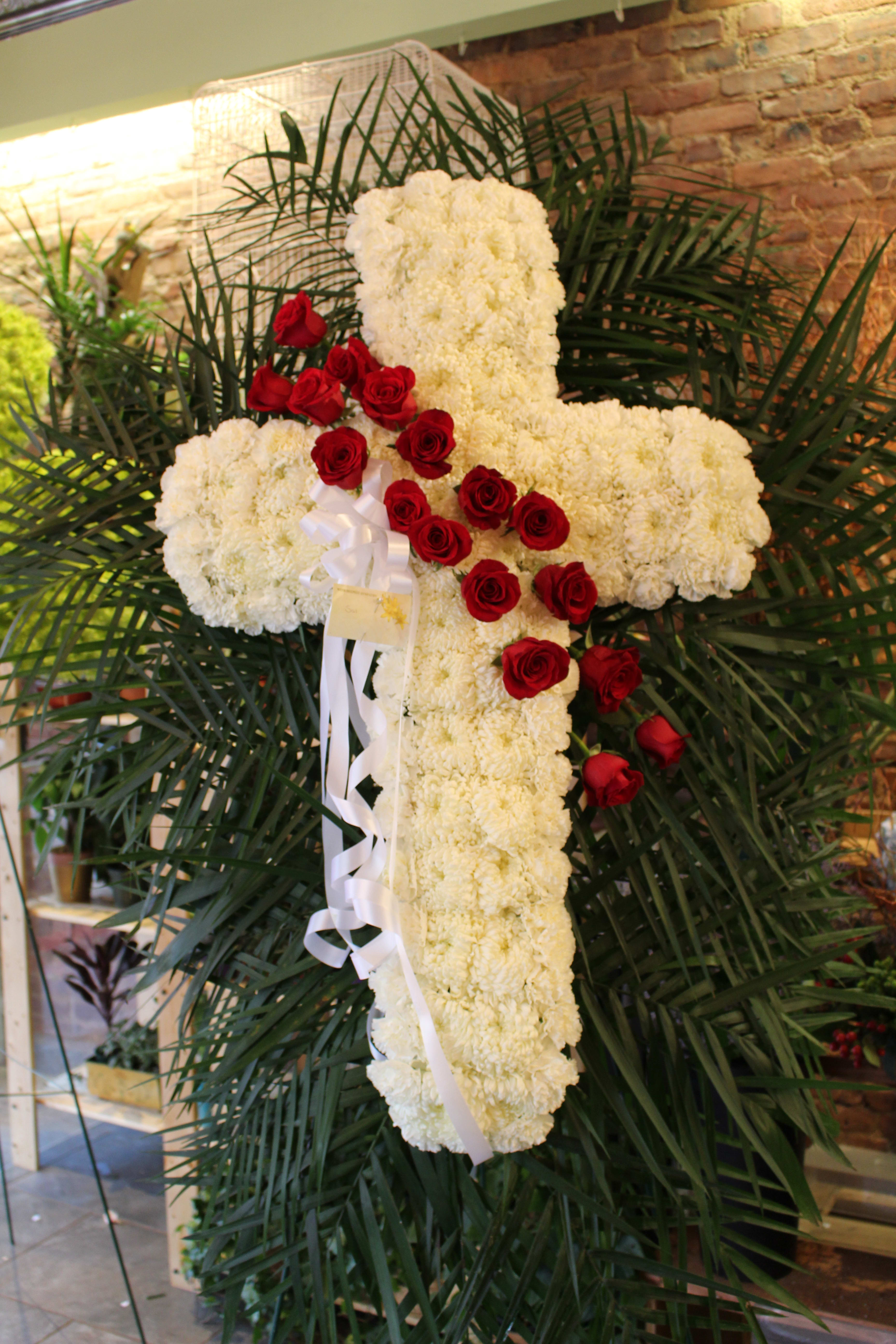 White floral cross with red roses and a white ribbon