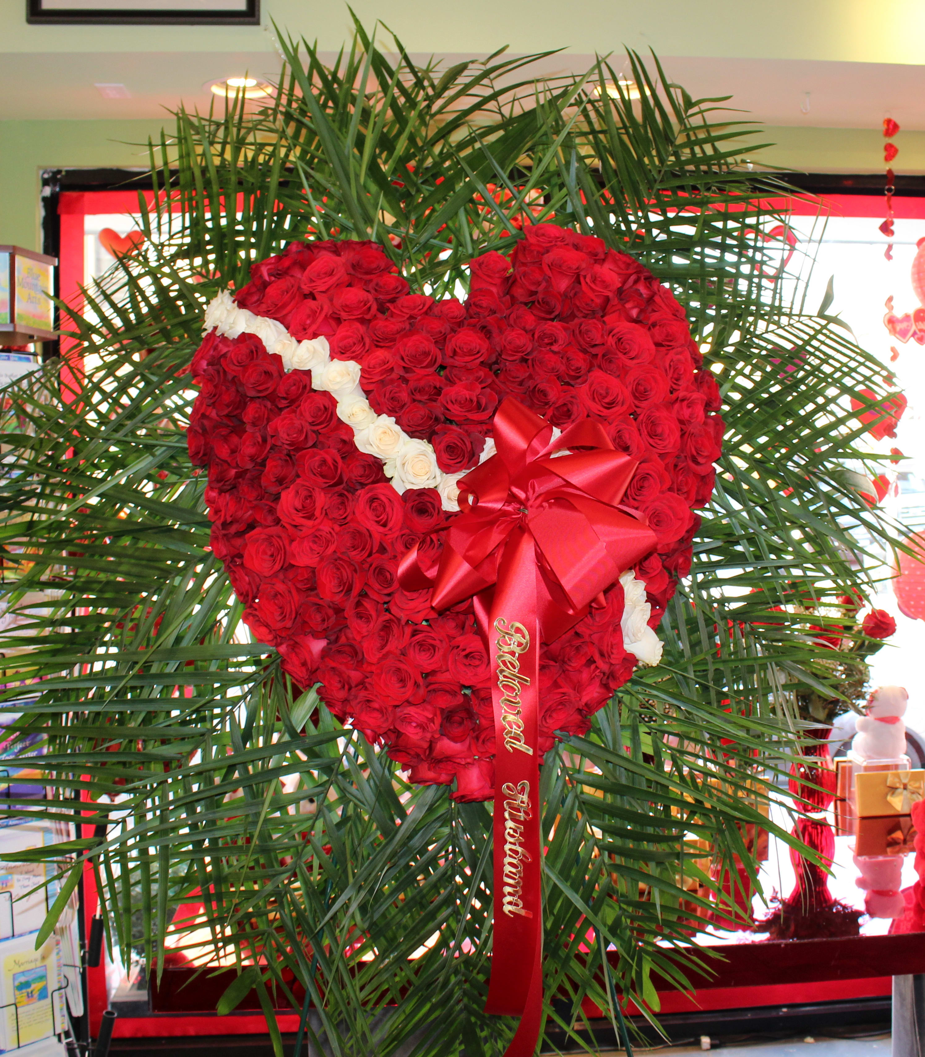 Heart-shaped red rose arrangement with a red ribbon and white rose accents