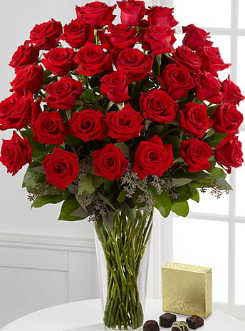 Bouquet of red roses in a clear glass vase with a box of chocolates