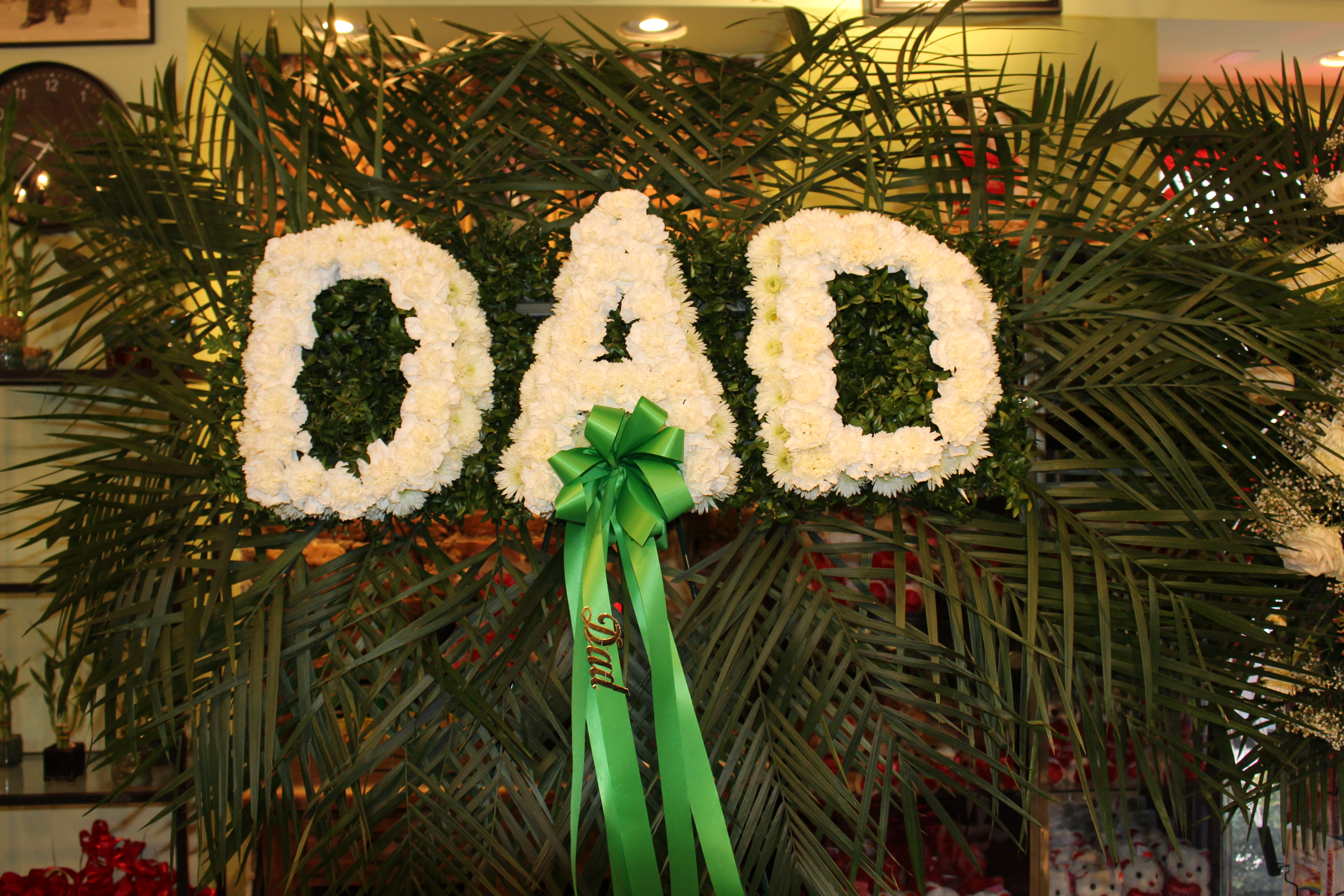 White floral letters spelling DAD with a green ribbon bow