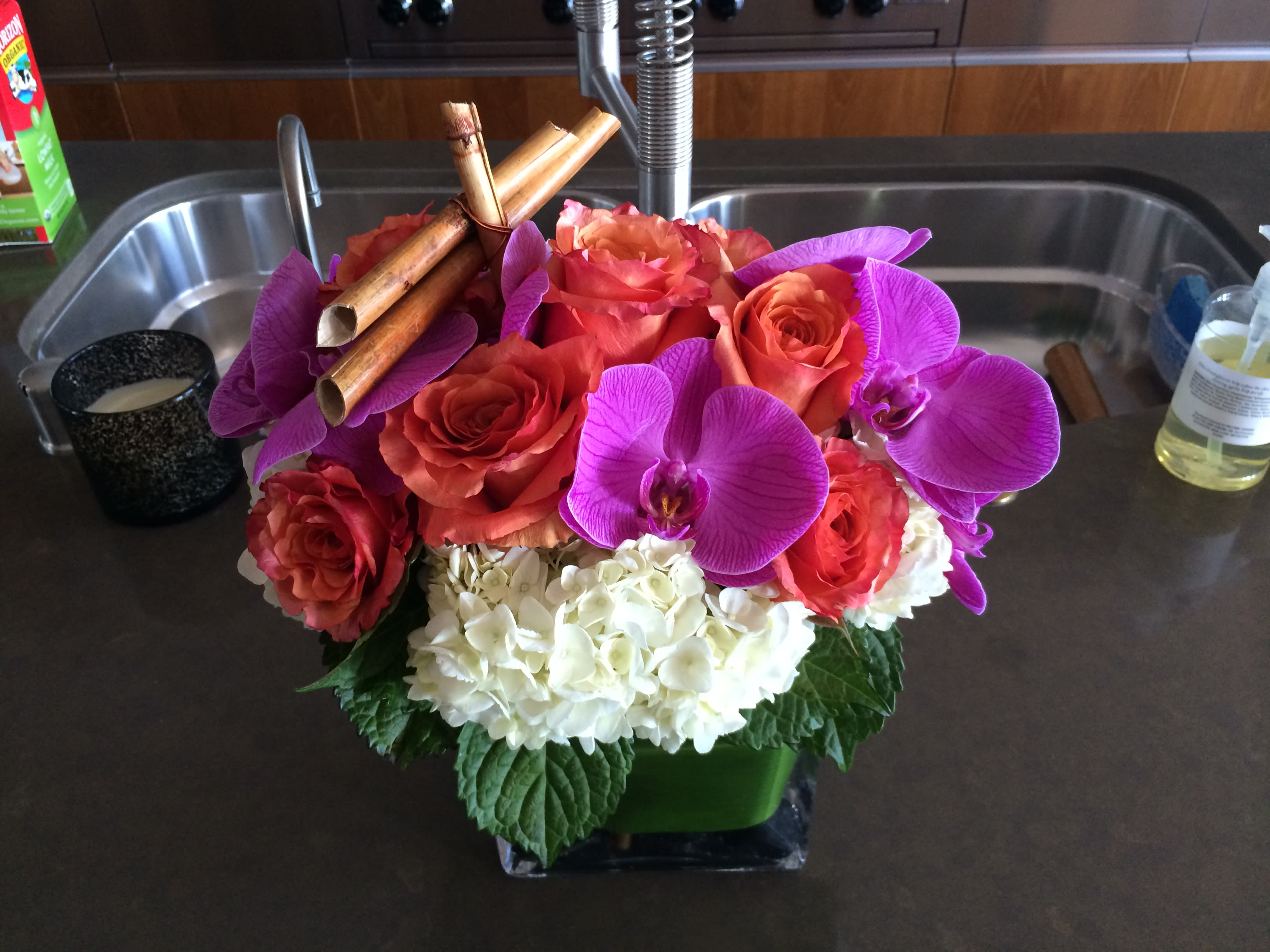 Bouquet of orange roses, purple orchids, and white hydrangeas in a square vase
