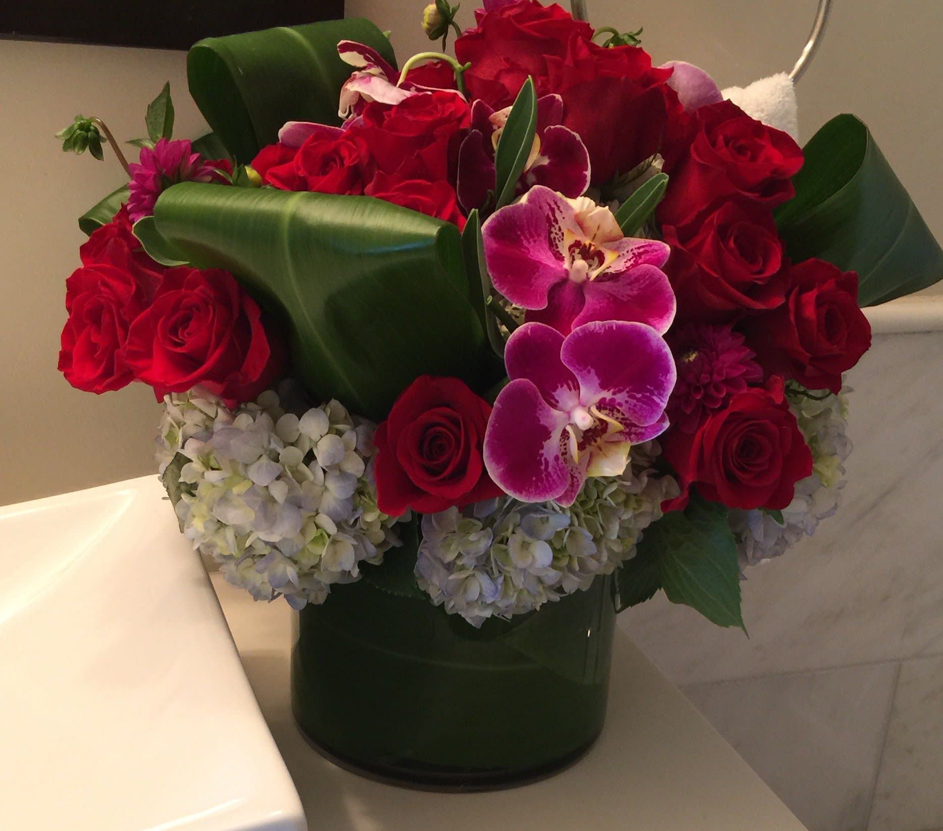Red roses and purple orchids in a dark green vase