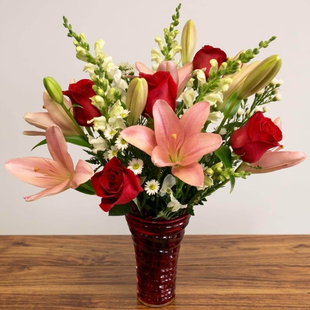 Red roses and pink lilies arranged in a red glass vase