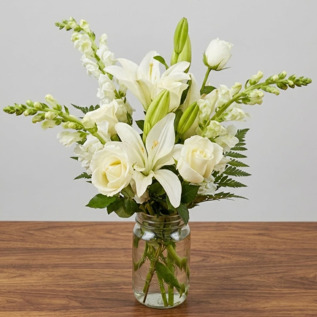 White lilies and roses arranged in a clear glass jar vase