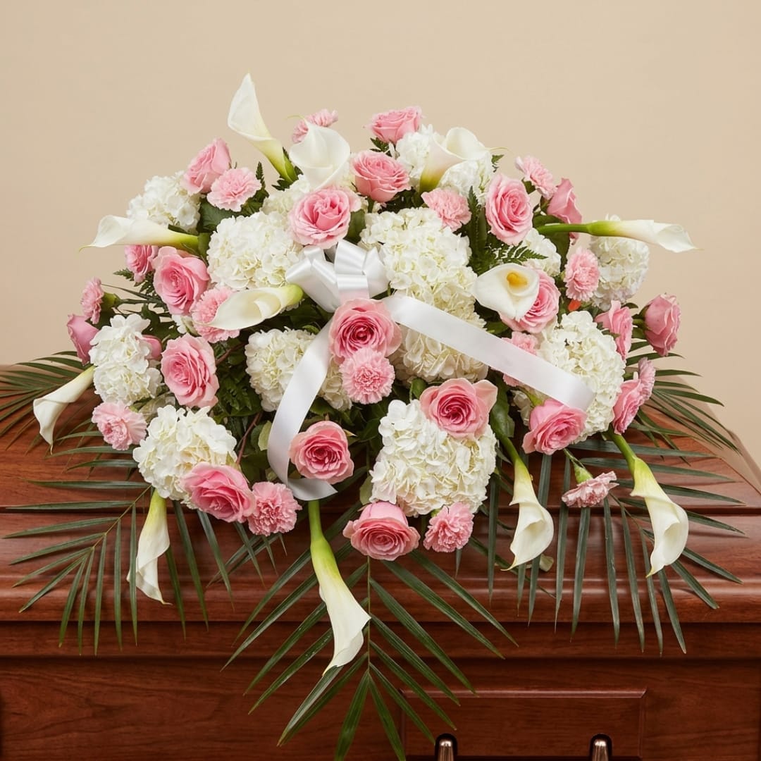 Pink roses and white calla lilies arranged with hydrangeas and a white ribbon