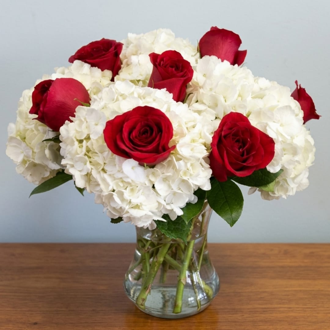 Red roses and white hydrangeas arranged in a clear glass vase