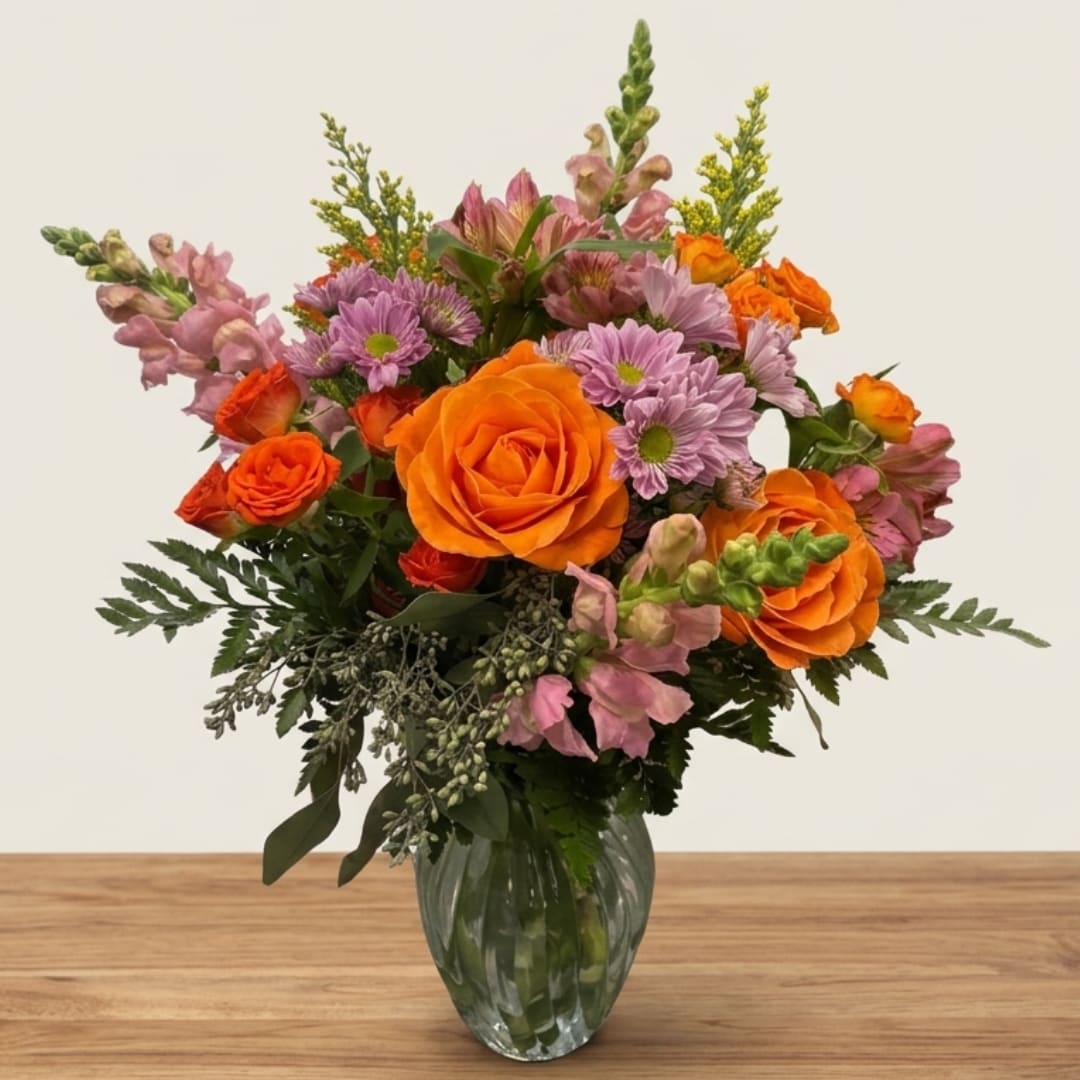 Orange roses and lavender daisies in a clear glass vase