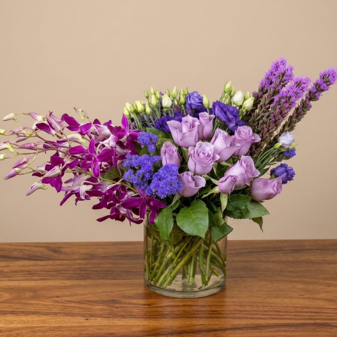 Purple orchid and rose bouquet in a clear glass vase