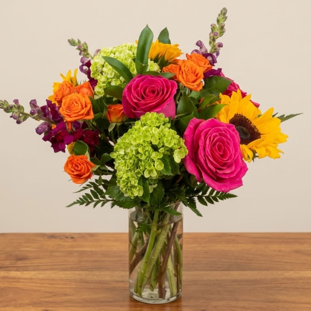 Mixed bouquet of roses, sunflowers, and green hydrangeas in a glass vase