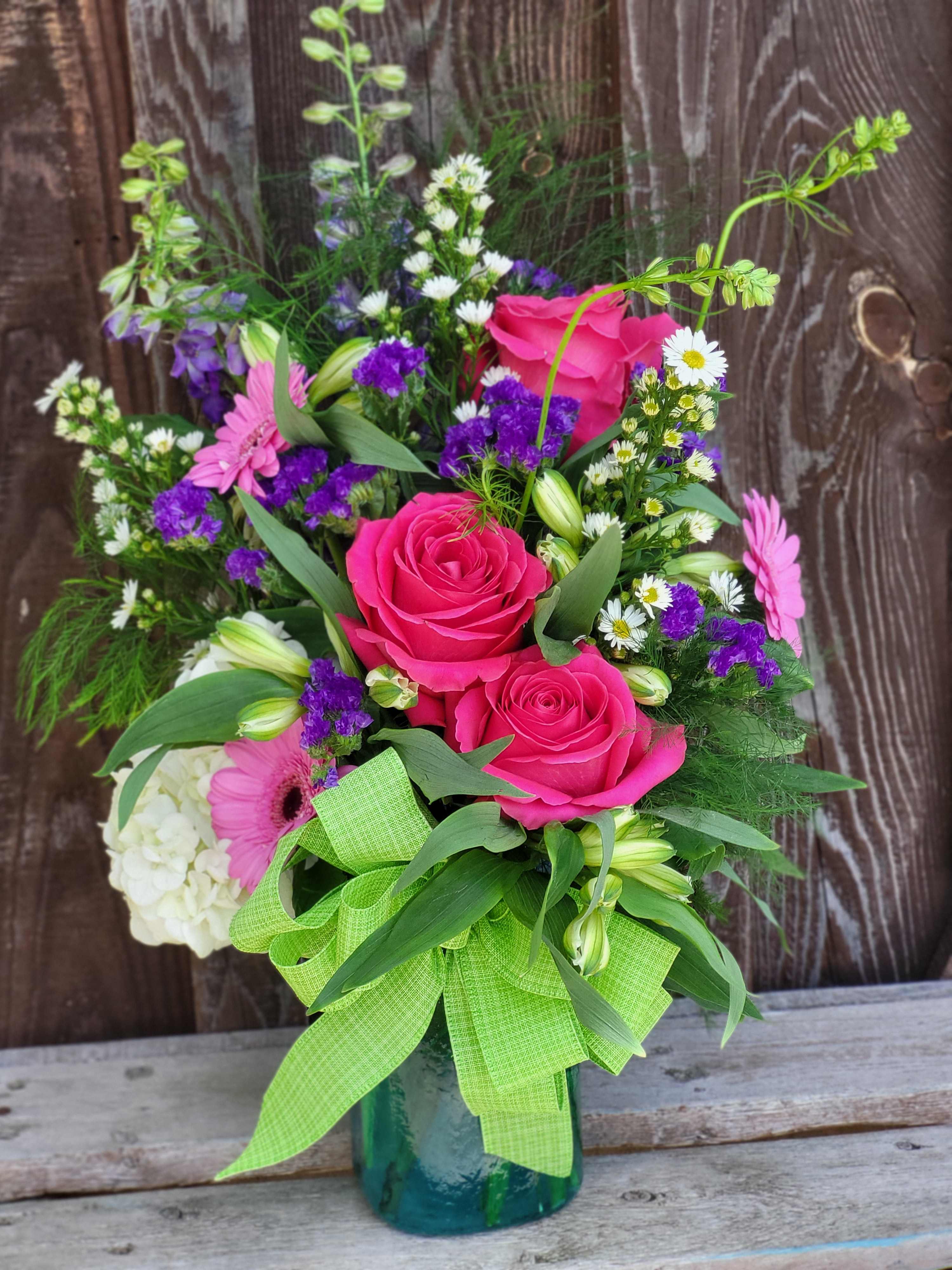 Pink roses and mixed flowers in a glass vase with a green ribbon