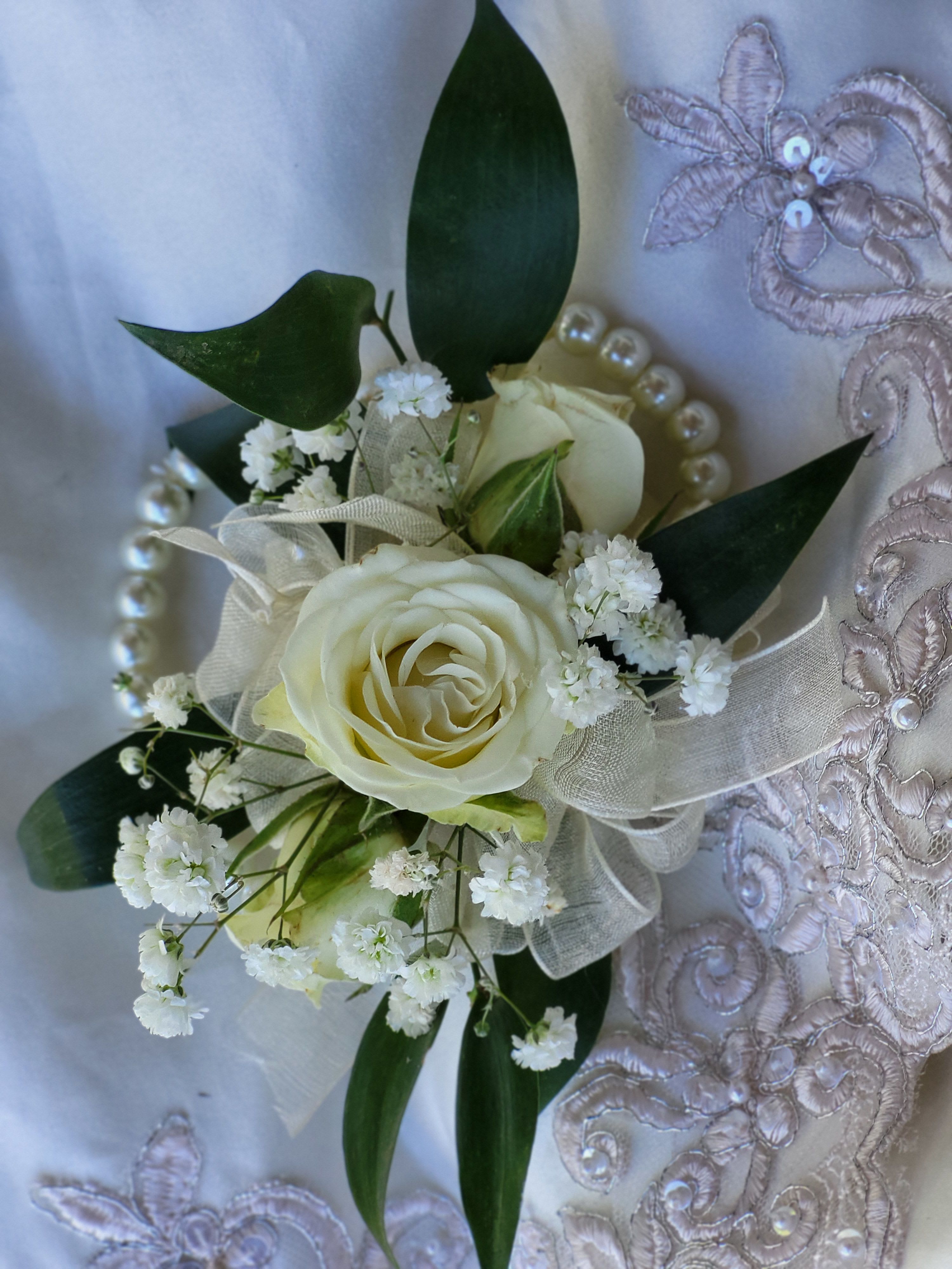 White rose corsage with baby's breath and dark green leaves